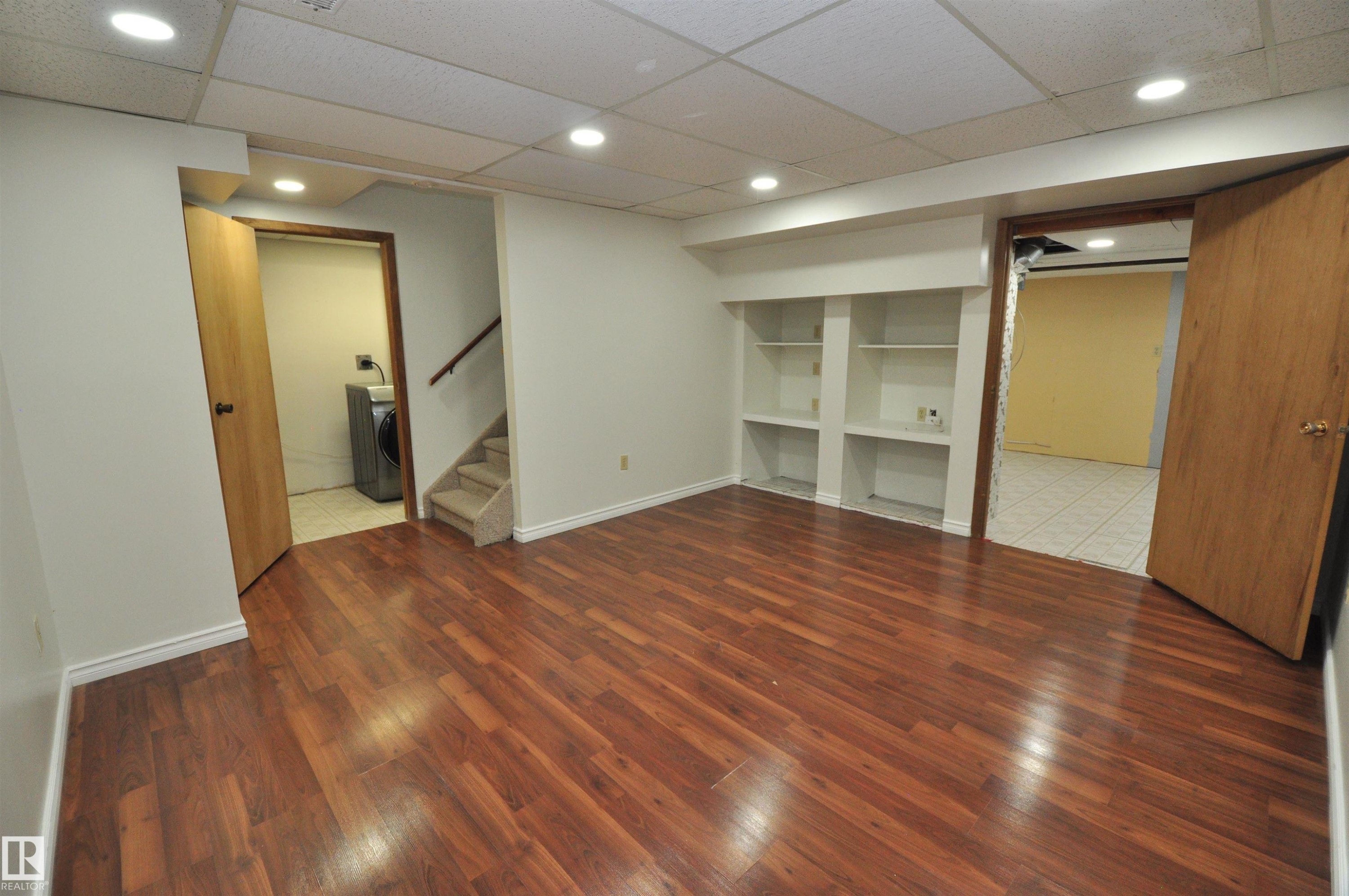 Spacious finished area featuring wood-finish flooring, recessed lighting, built-in shelving, and white baseboards - 617 Millbourne Road E, Edmonton, AB