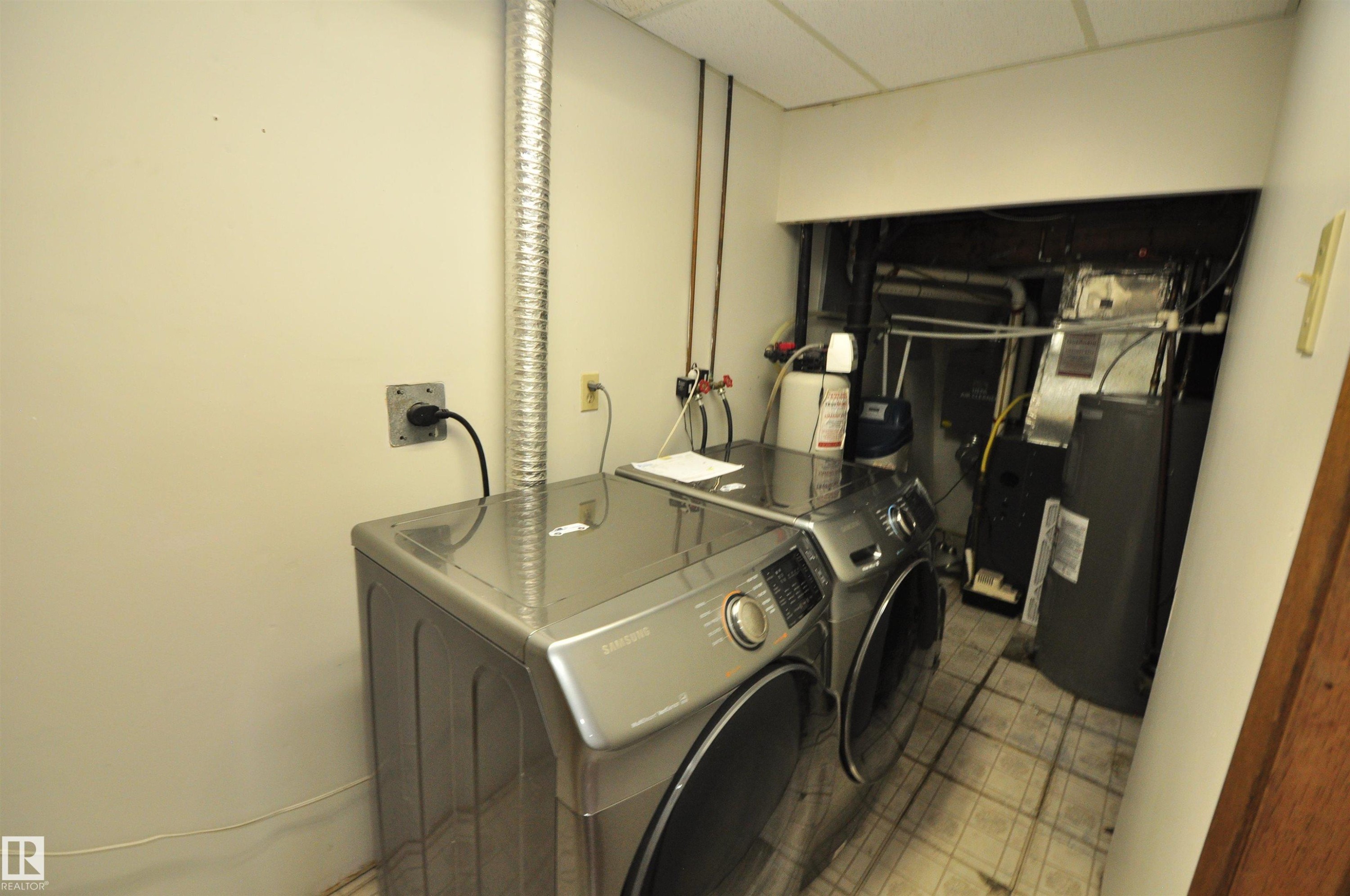 Dedicated utility area featuring a front-loading washer and dryer, tiled flooring, exposed ductwork, and essential mechanical systems - 617 Millbourne Road E, Edmonton, AB