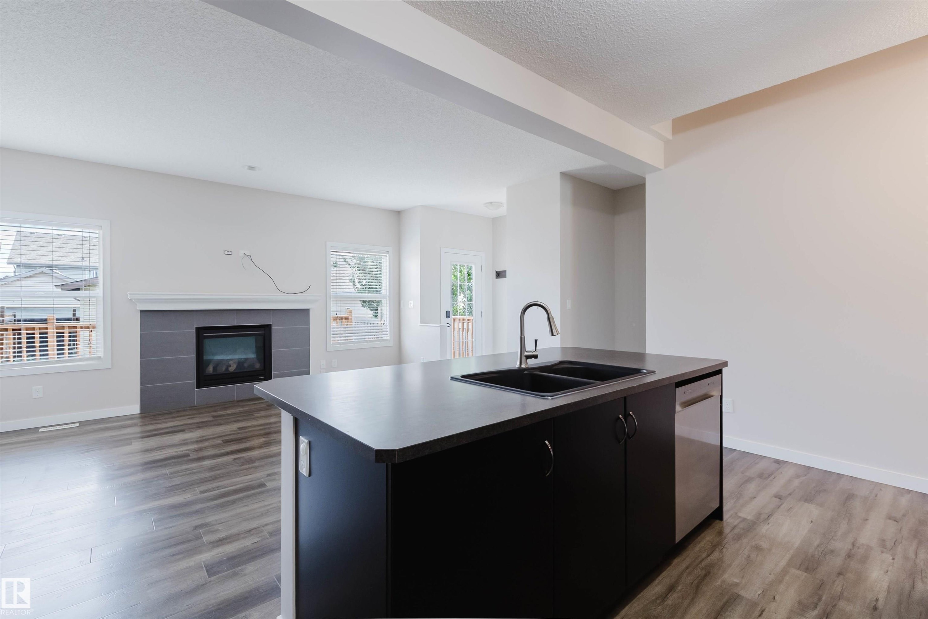 Kitchen island featuring a double-basin sink with a gooseneck faucet, integrated dishwasher, and dark cabinetry - 636 Mcdonough Link Link, Edmonton, AB