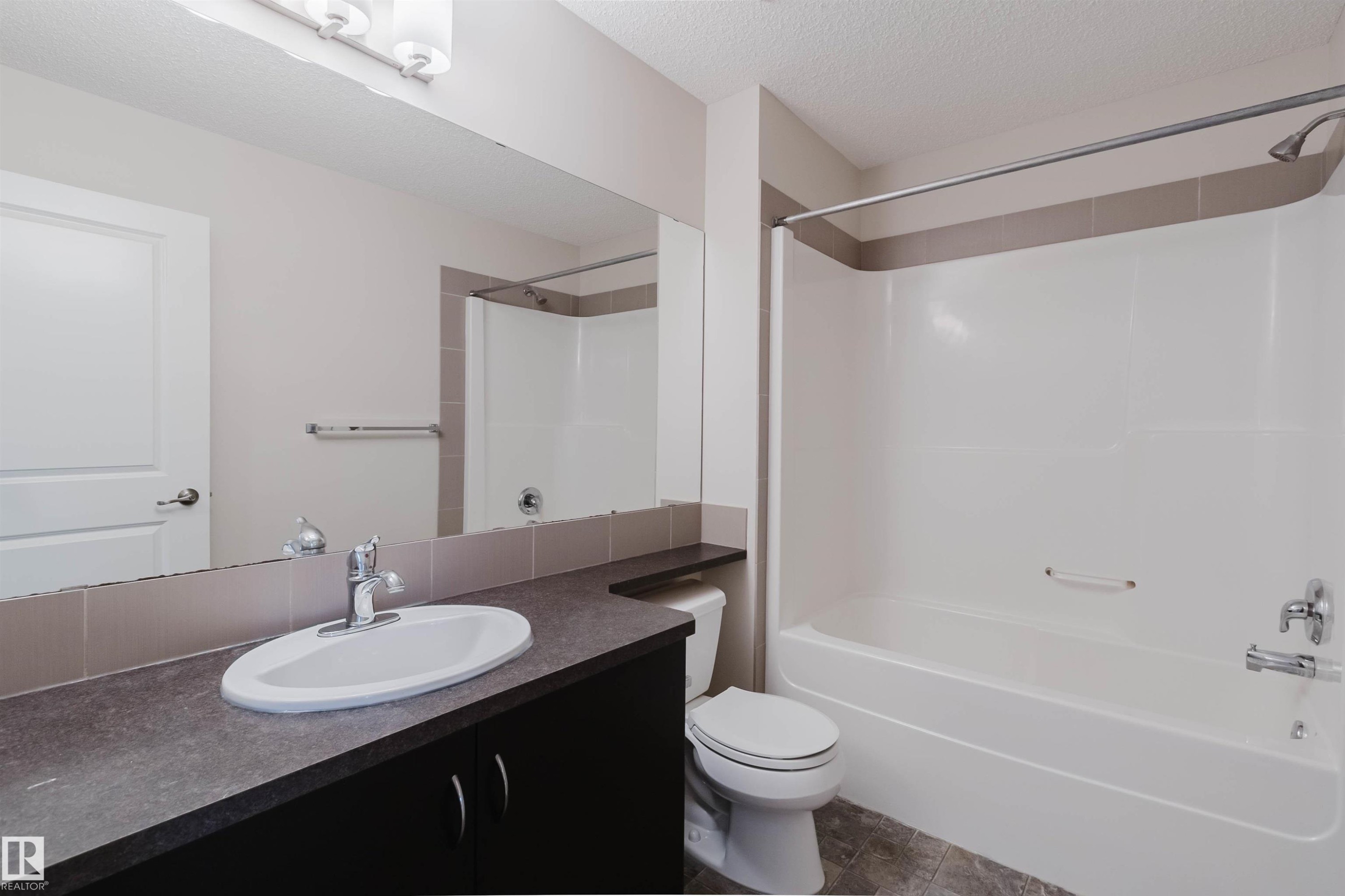 Bathroom featuring a white bathtub with shower, dark vanity with integrated sink, chrome fixtures, and a large wall-mounted mirror - 636 Mcdonough Link Link, Edmonton, AB