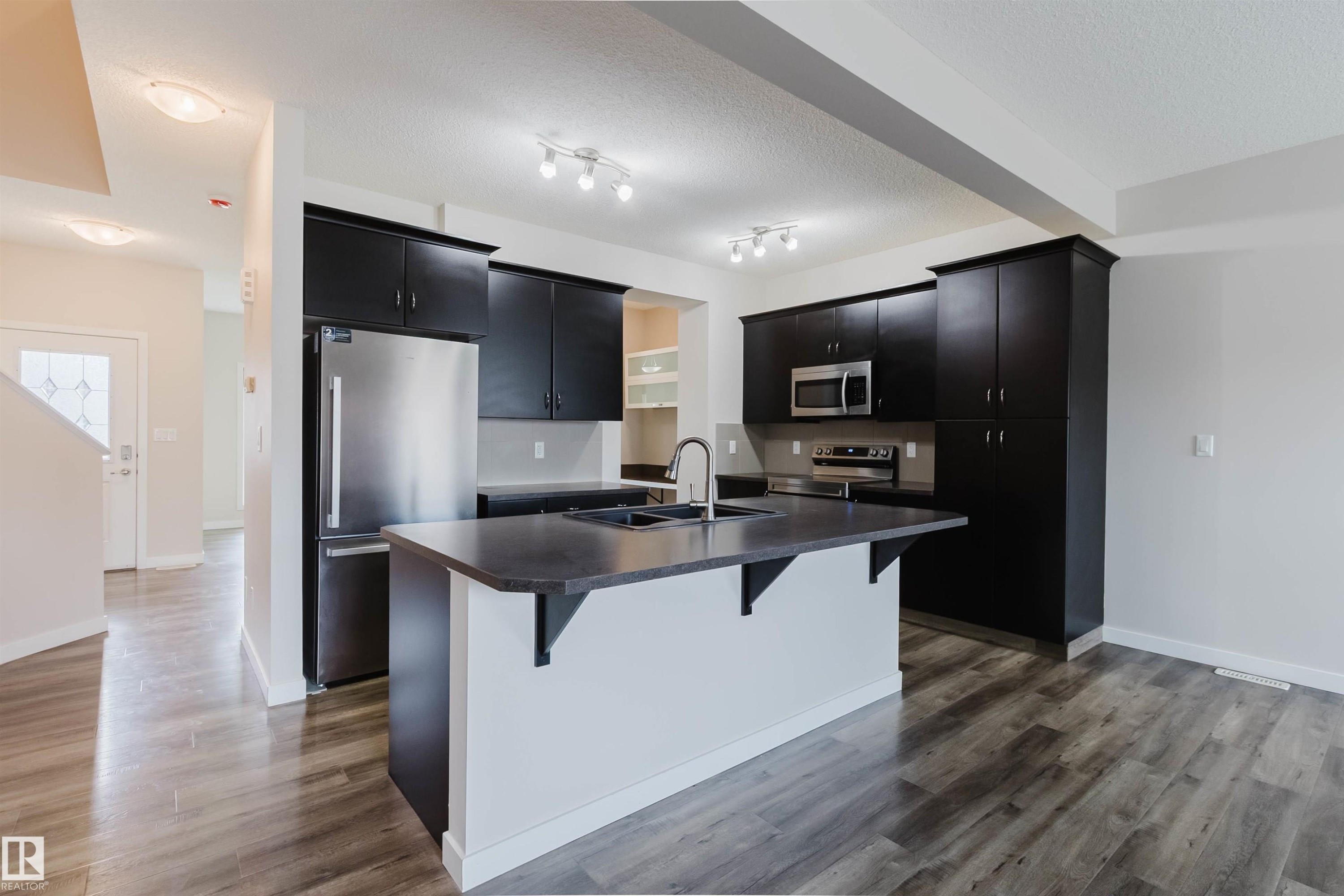 Modern kitchen featuring dark cabinetry, stainless steel appliances, and a central island with an undermount sink - 636 Mcdonough Link Link, Edmonton, AB