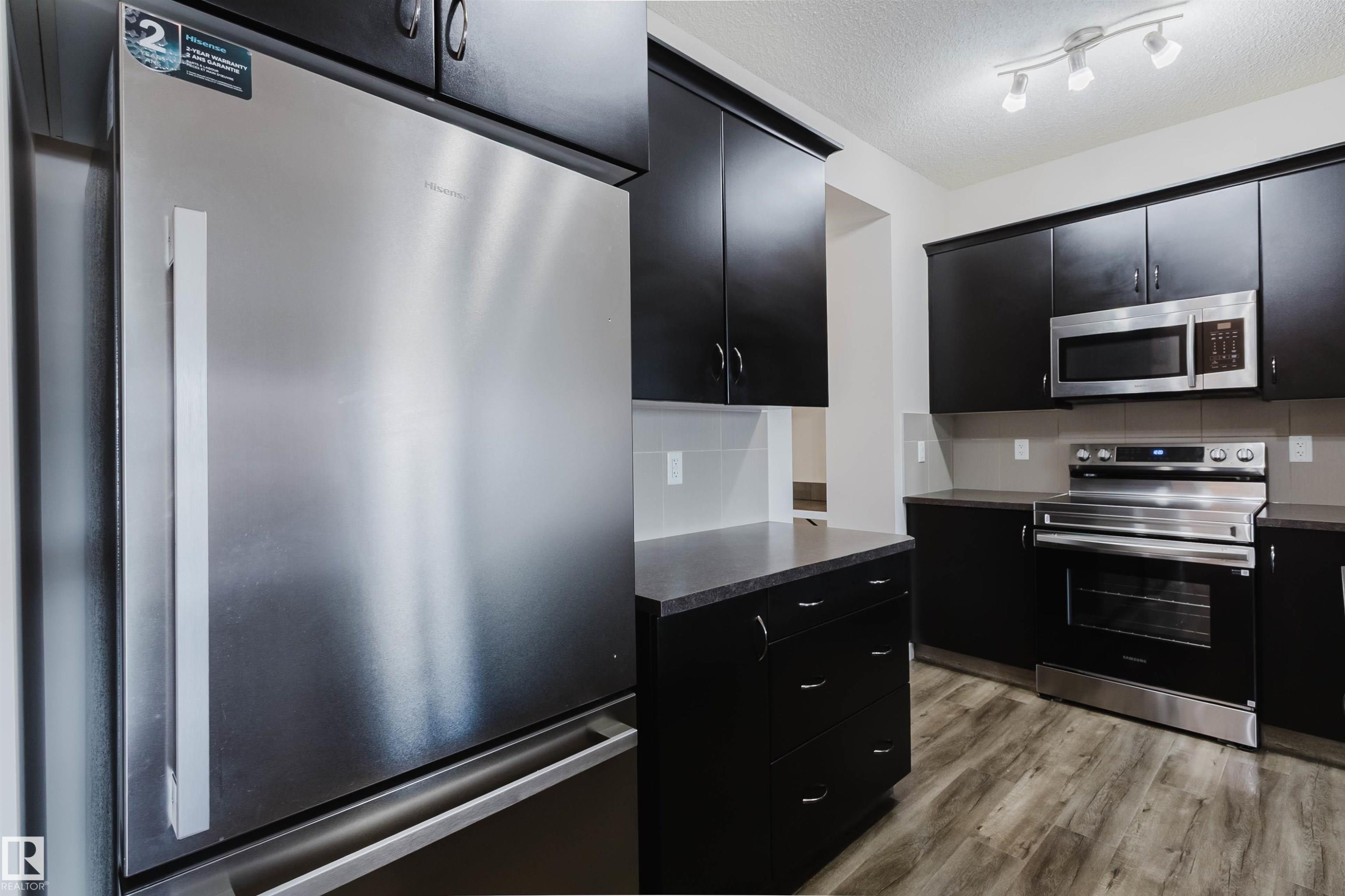 Kitchen featuring stainless steel appliances, dark cabinetry, light countertops, and wood-finish flooring - 636 Mcdonough Link Link, Edmonton, AB