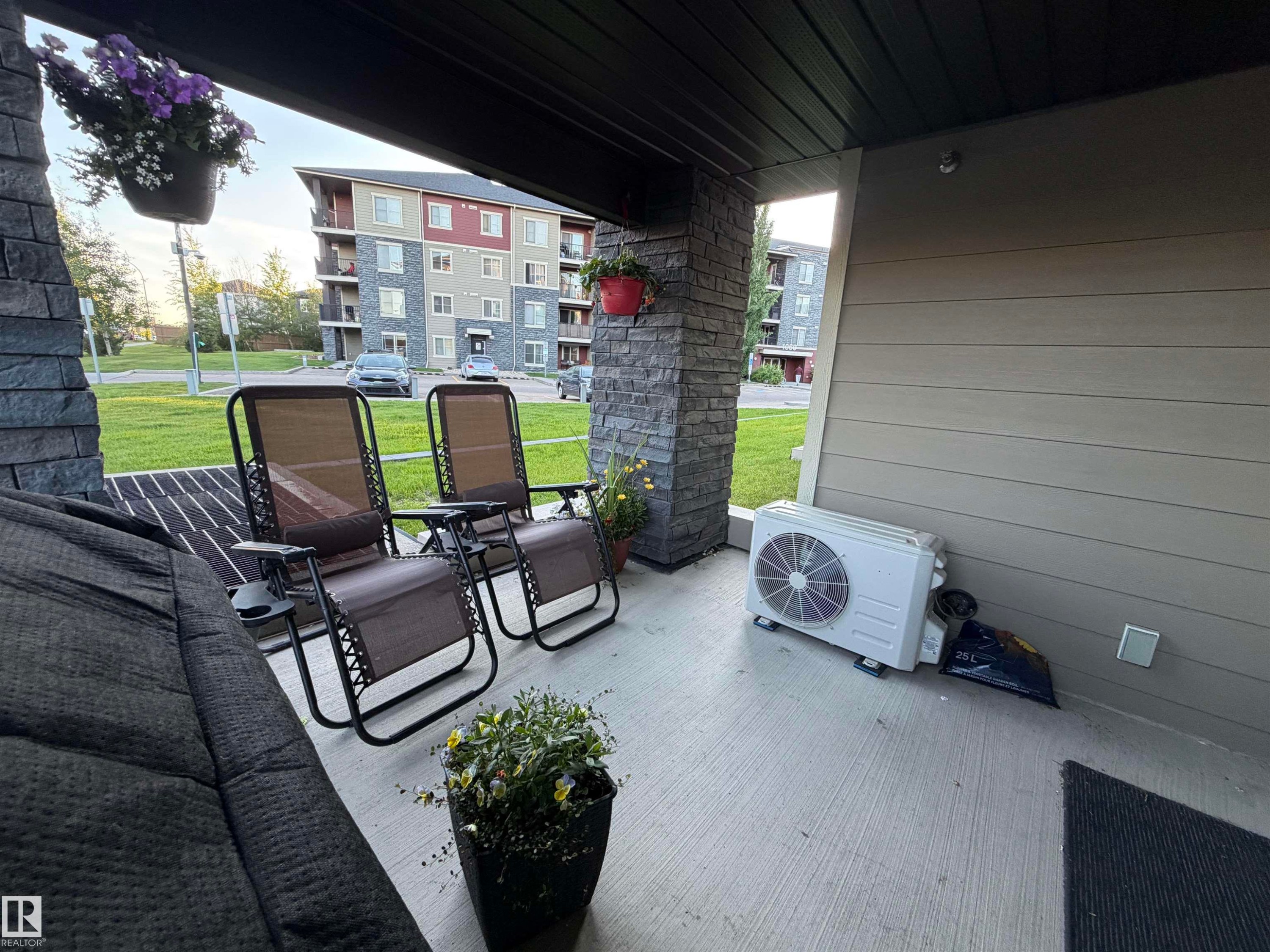 Covered concrete patio featuring stone veneer pillars, horizontal siding, and a slatted ceiling - 114 1080 Mcconachie Boulevard, Edmonton, AB