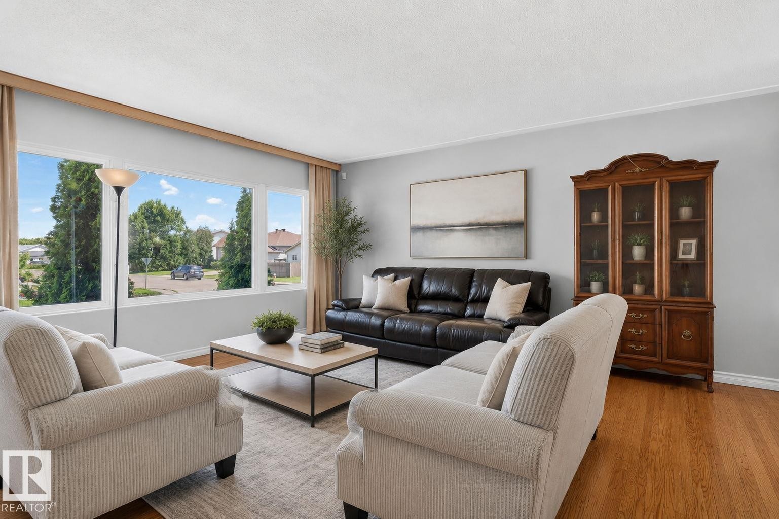 Spacious living area featuring expansive windows, wood-finish flooring, light gray wall tones, and a built-in display cabinet - 12238 48 Street, Edmonton, AB