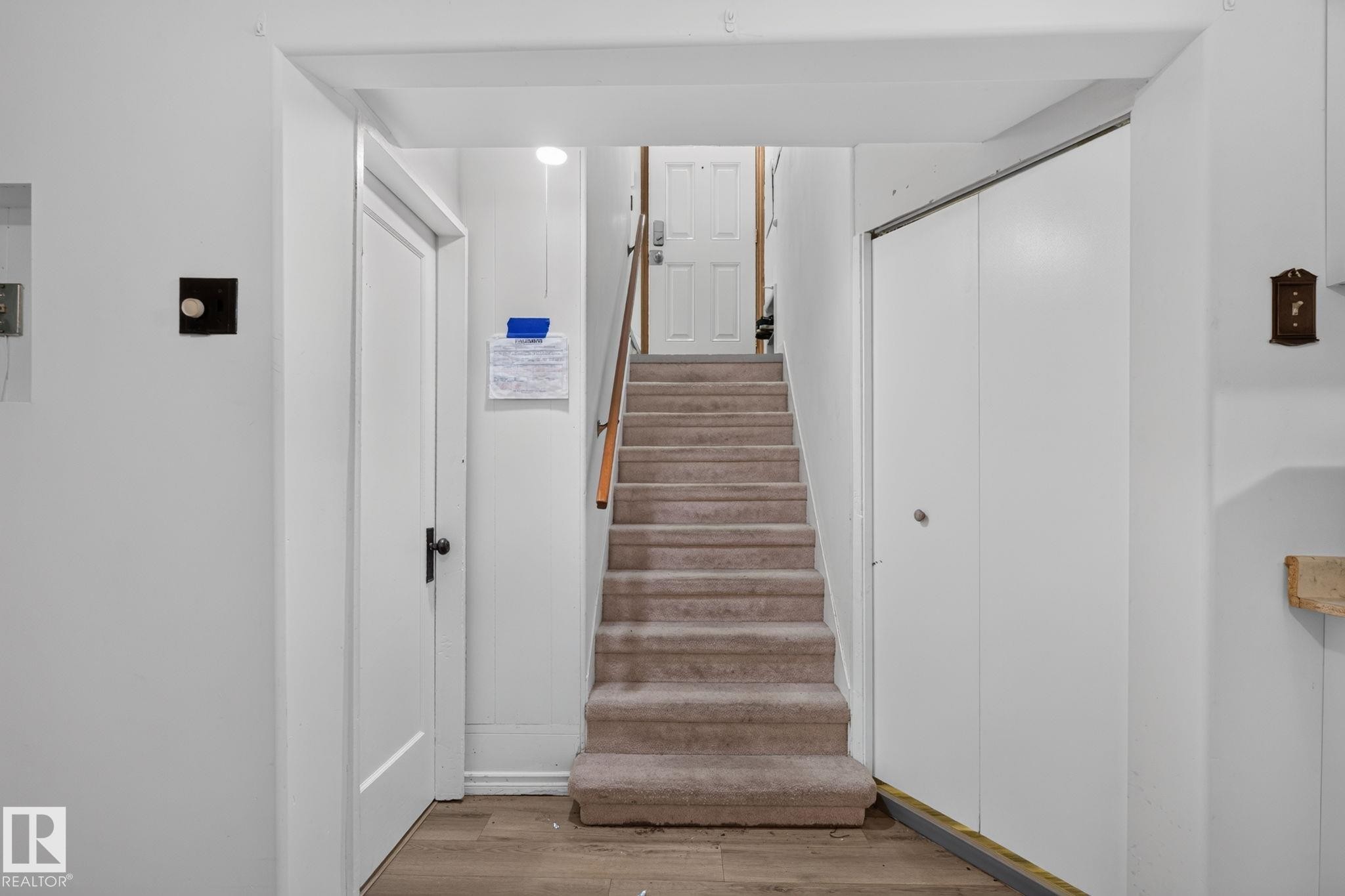 Carpeted staircase with wood railing, flanked by a white door with black hardware and white bi-fold closet doors - 12238 48 Street, Edmonton, AB