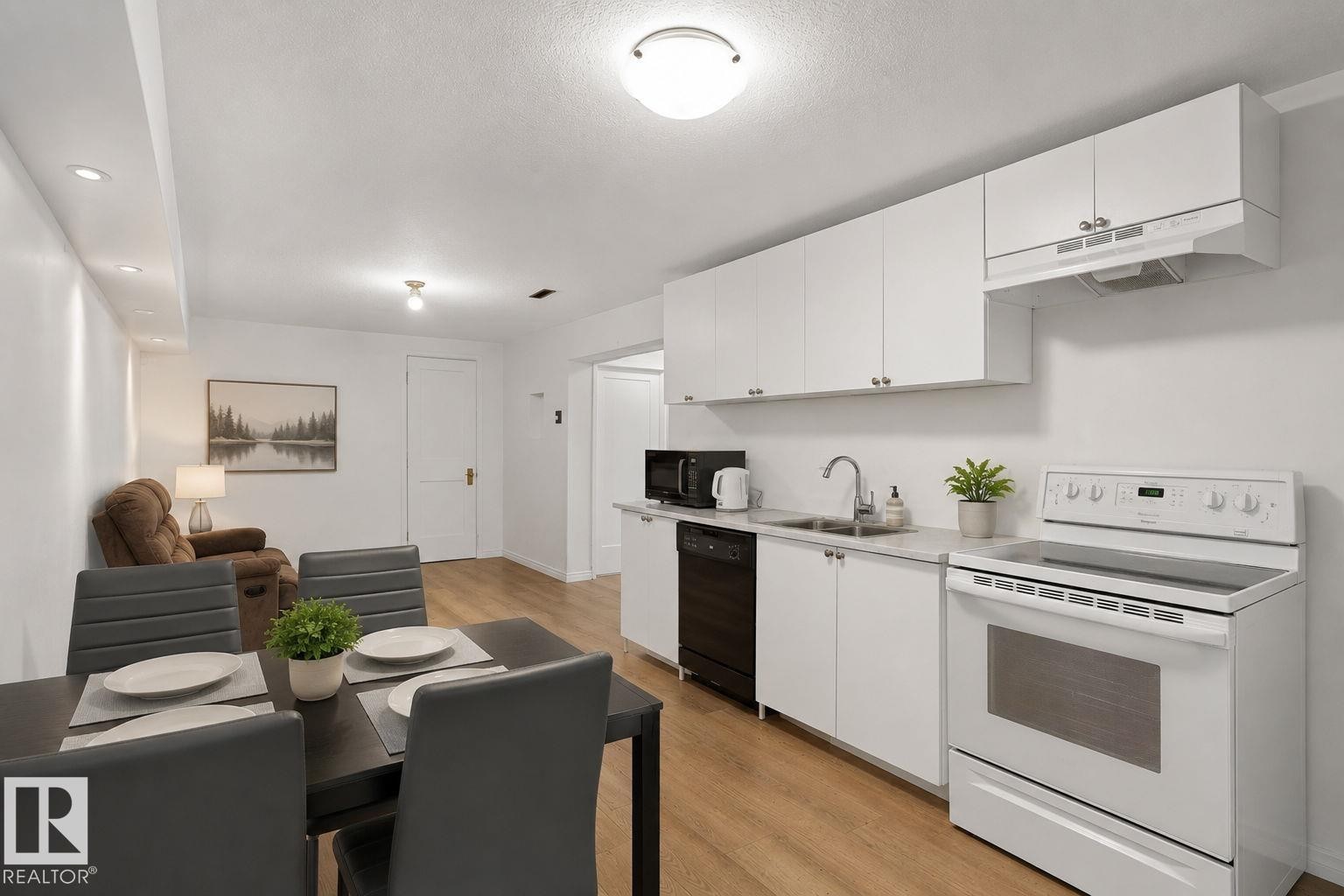 Open-concept living area featuring a modern kitchen with white cabinetry and appliances, wood-finish flooring, recessed lighting, and a dining area - 12238 48 Street, Edmonton, AB