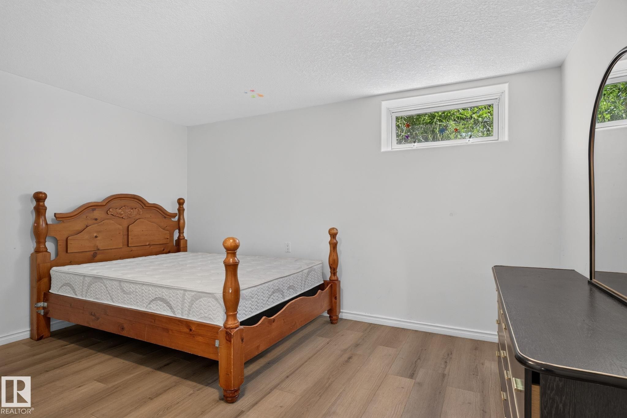 Room featuring wood-finish flooring, a neutral color palette on walls, and a horizontal window providing natural light - 12238 48 Street, Edmonton, AB