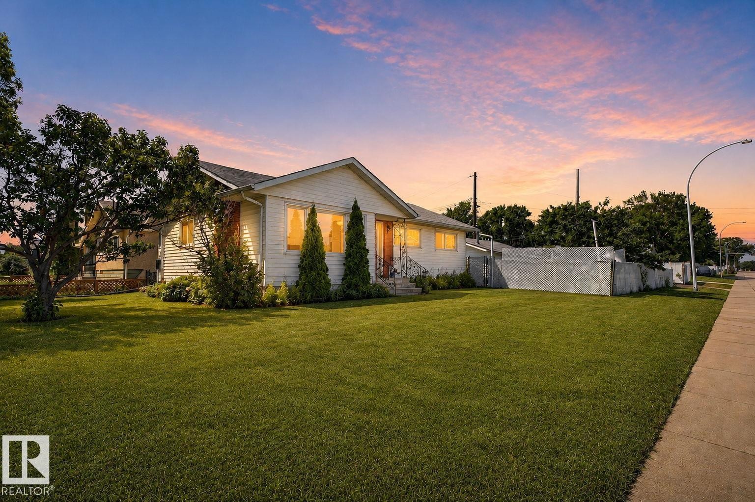 White siding exterior with a front-facing gable, featuring a manicured lawn, established trees, and a concrete sidewalk - 12238 48 Street, Edmonton, AB