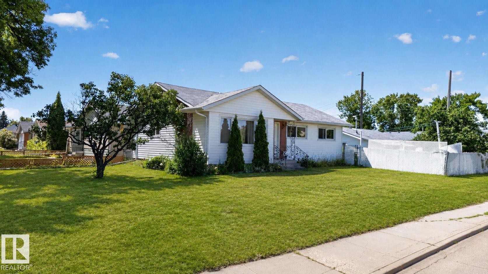 Single-story home featuring white siding, a dark shingle roof, and a prominent front lawn - 12238 48 Street, Edmonton, AB