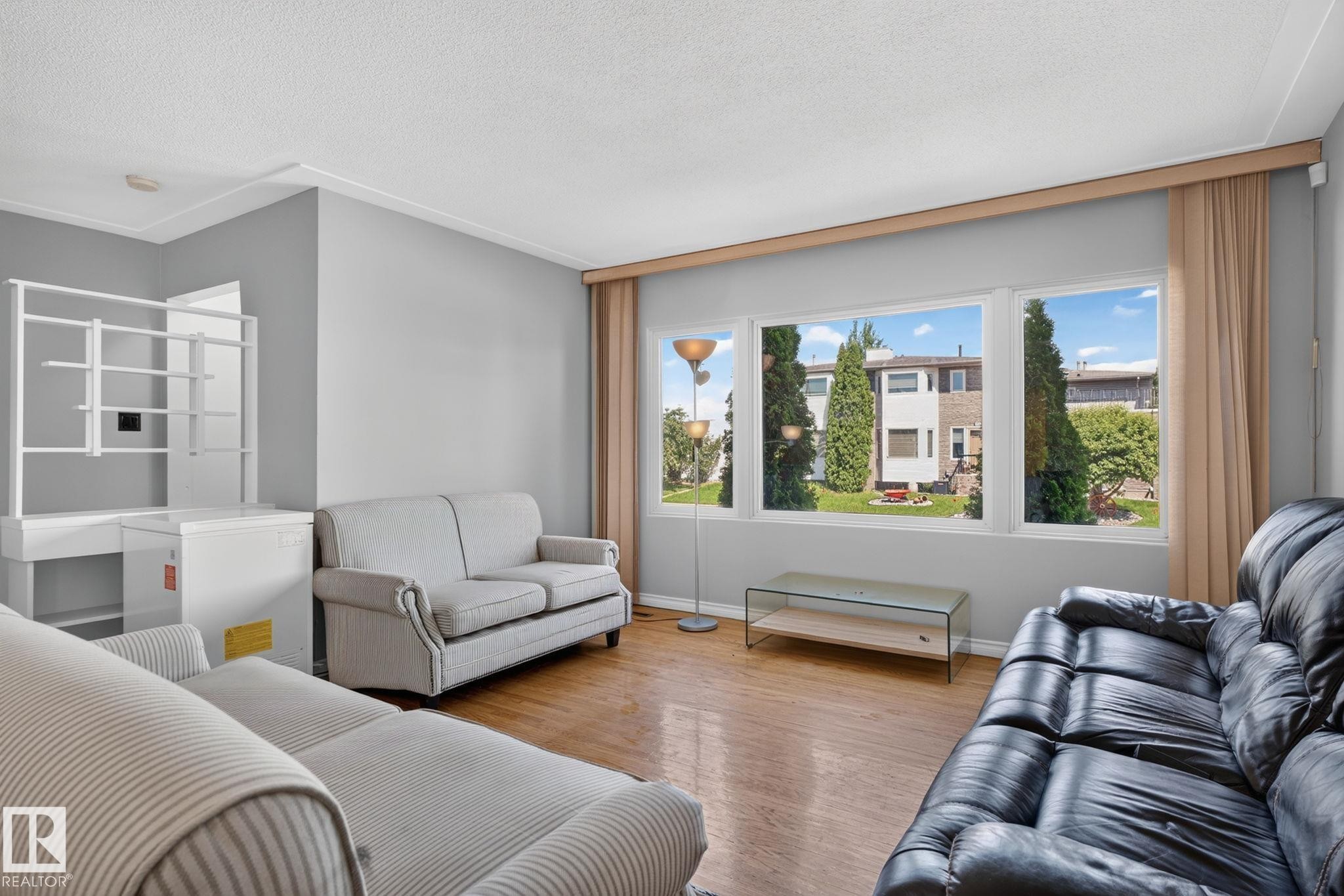 Living area featuring wood-finish flooring, a neutral wall color, crown molding, and large windows with privacy drapes - 12238 48 Street, Edmonton, AB
