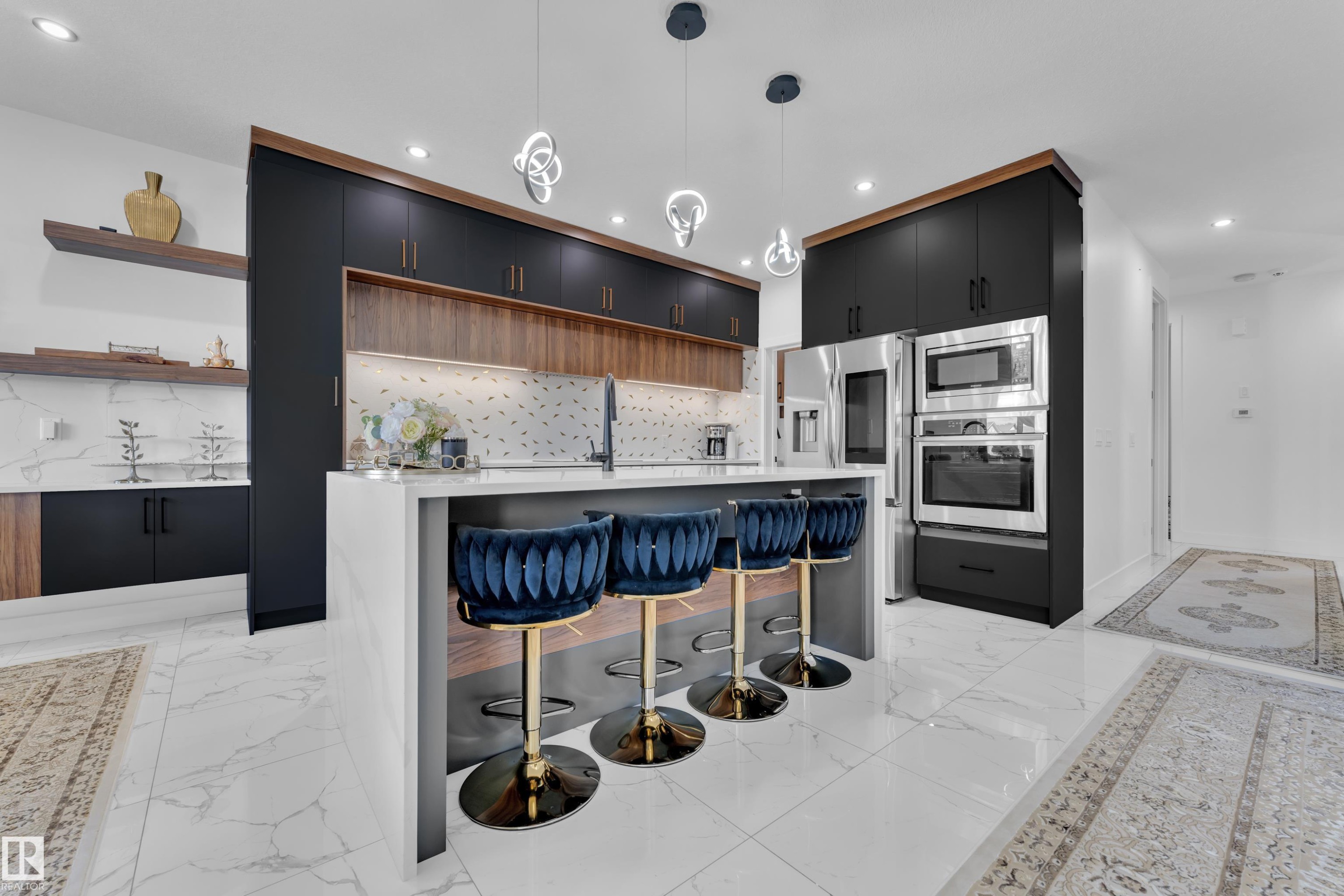 Modern kitchen featuring a waterfall island, sleek black cabinetry with wood accents, integrated stainless steel appliances, and distinctive pendant lighting - 16816 49 Street, Edmonton, AB