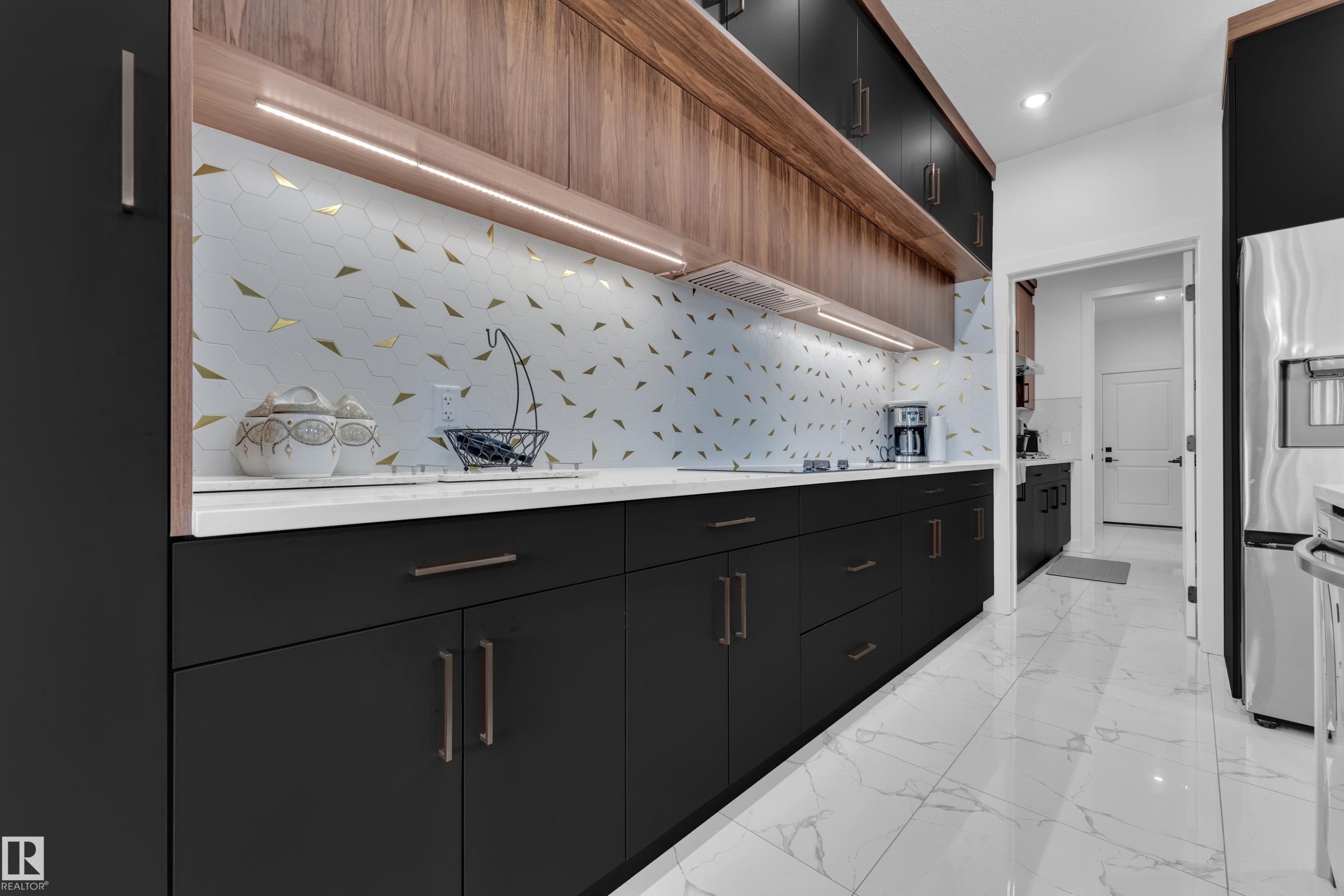 Modern kitchen featuring dark cabinetry with wood-finish accents, white countertops, and a patterned backsplash - 16816 49 Street, Edmonton, AB