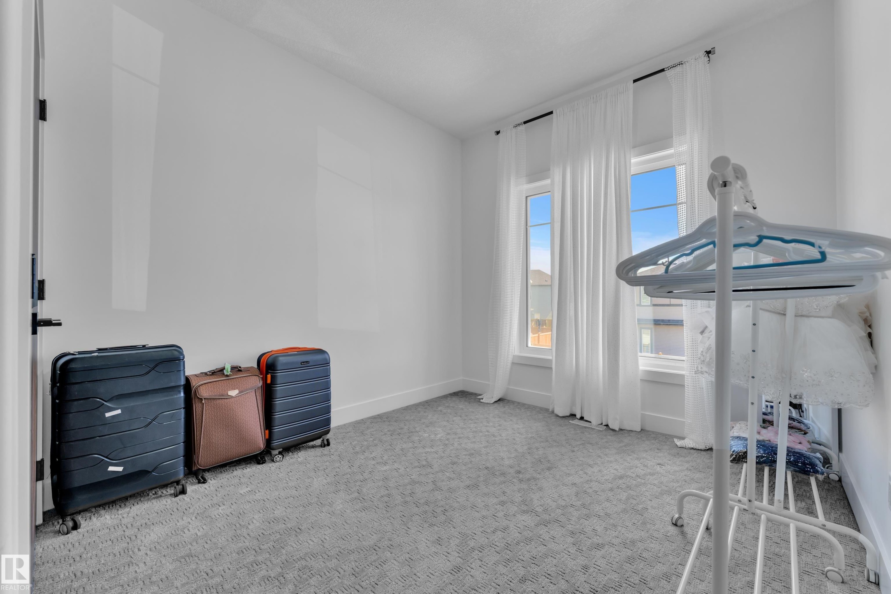 Bright interior space featuring two tall windows with sheer white drapery, white walls, and gray patterned carpet - 16816 49 Street, Edmonton, AB