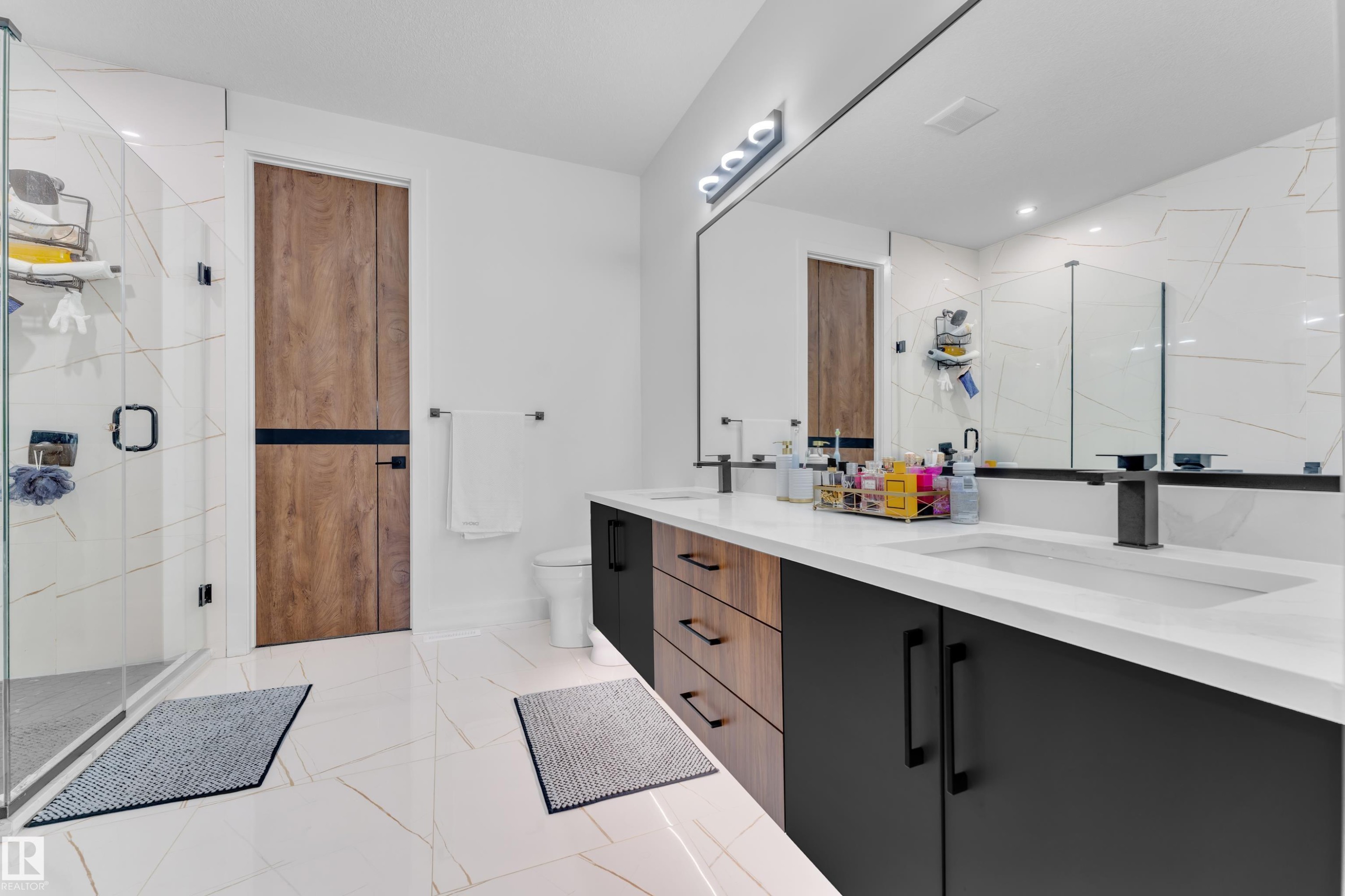 Dual vanity with black hardware and integrated sinks, a large wall-mounted mirror, and contemporary lighting - 16816 49 Street, Edmonton, AB