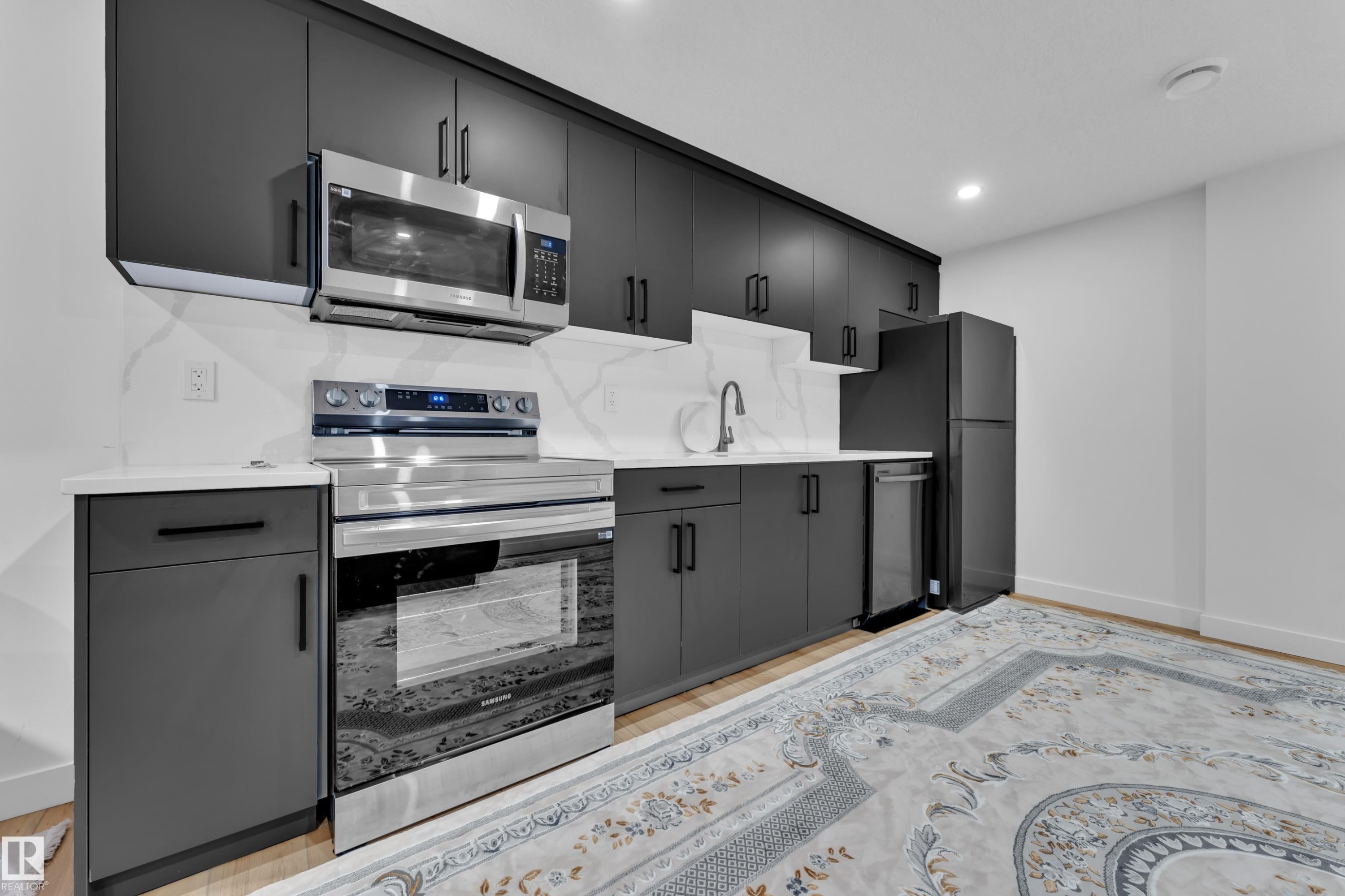 Modern kitchen featuring matte black cabinetry, stainless steel appliances, white countertops, and a white marble-patterned backsplash - 16816 49 Street, Edmonton, AB