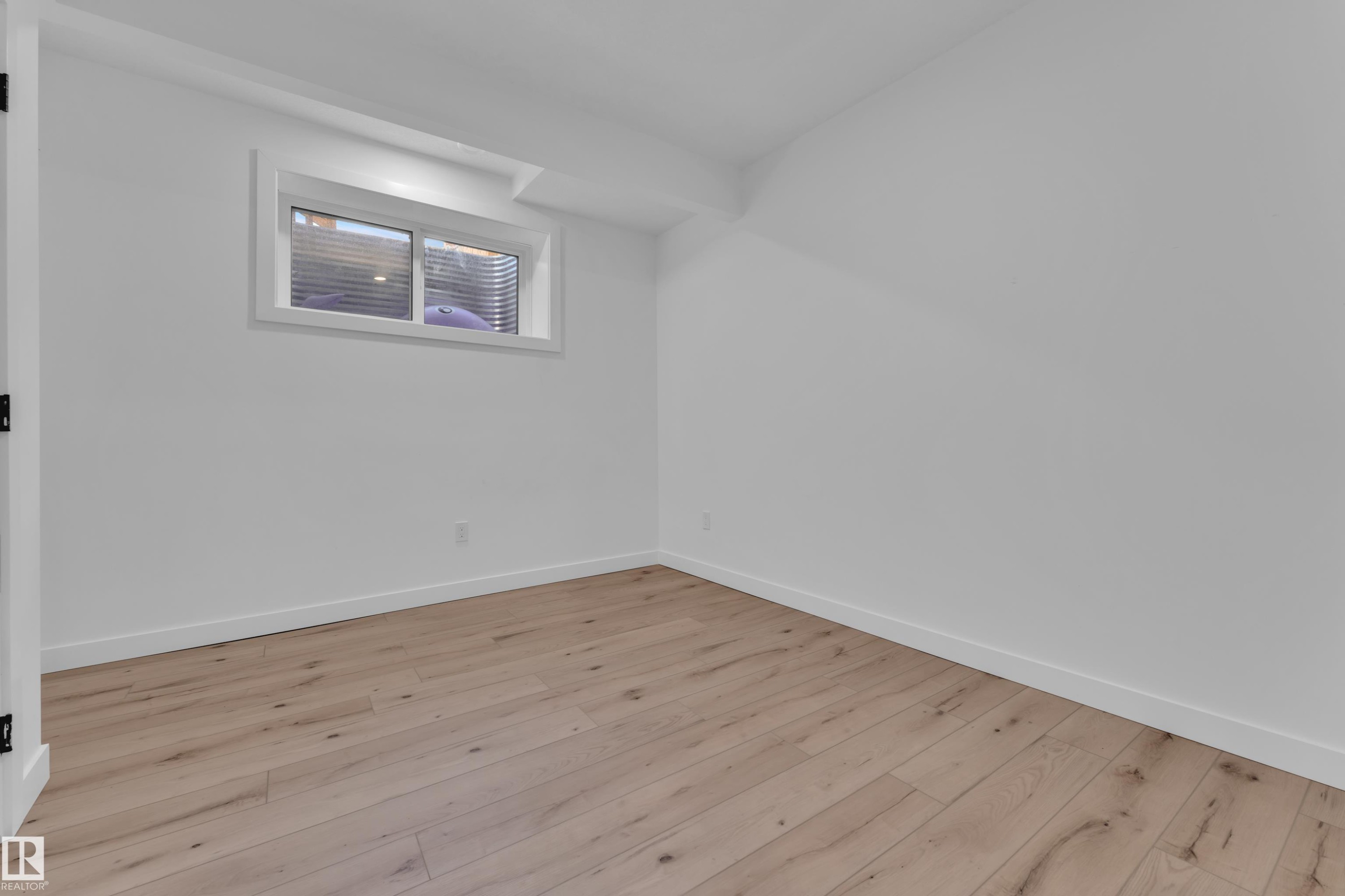Bright room featuring wood-finish flooring, white painted walls, crisp white baseboards, and a window with horizontal blinds - 16816 49 Street, Edmonton, AB