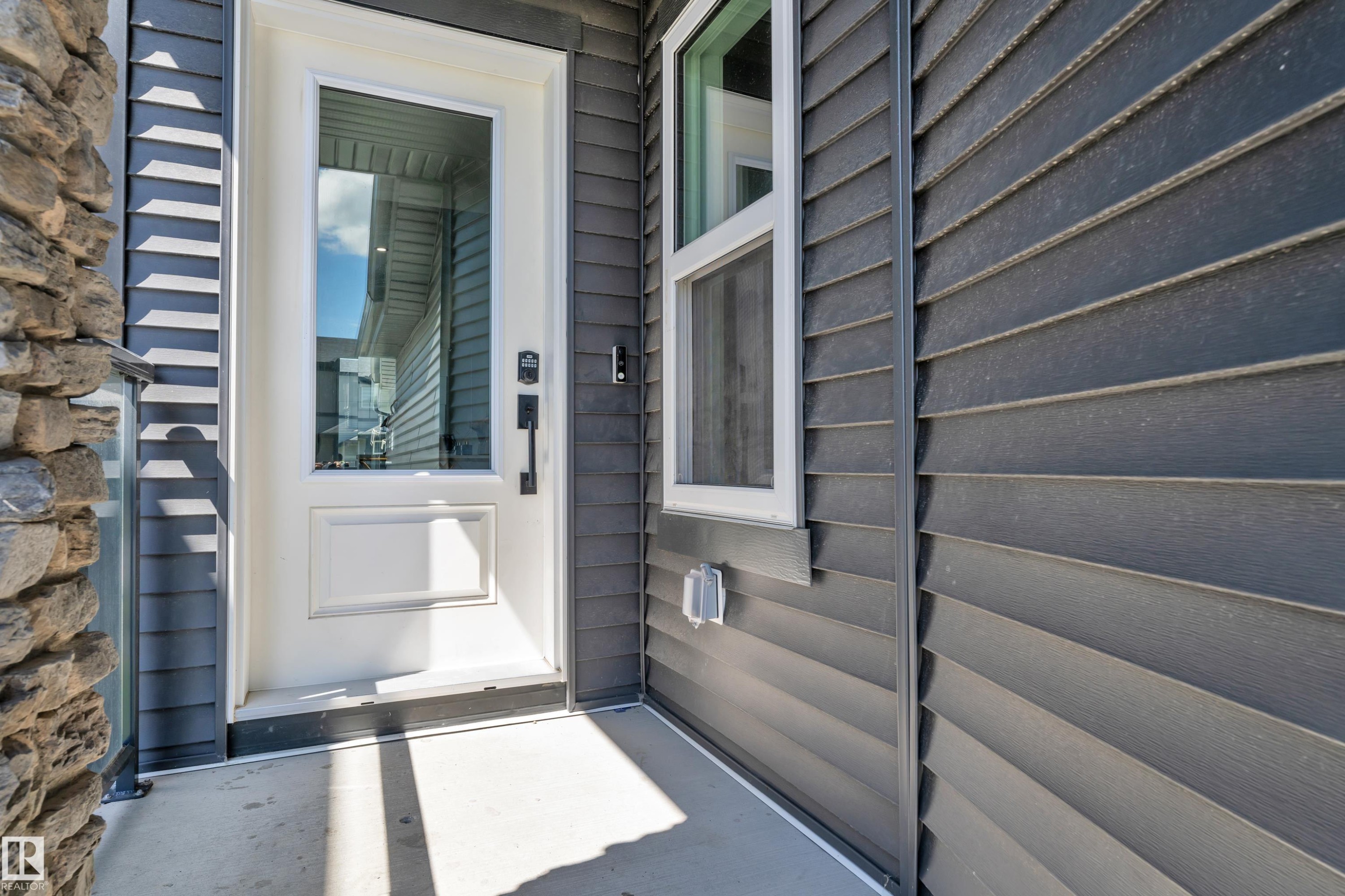 Entryway featuring a white door with an integrated glass panel, dark horizontal siding, and a partial stone facade - 16816 49 Street, Edmonton, AB
