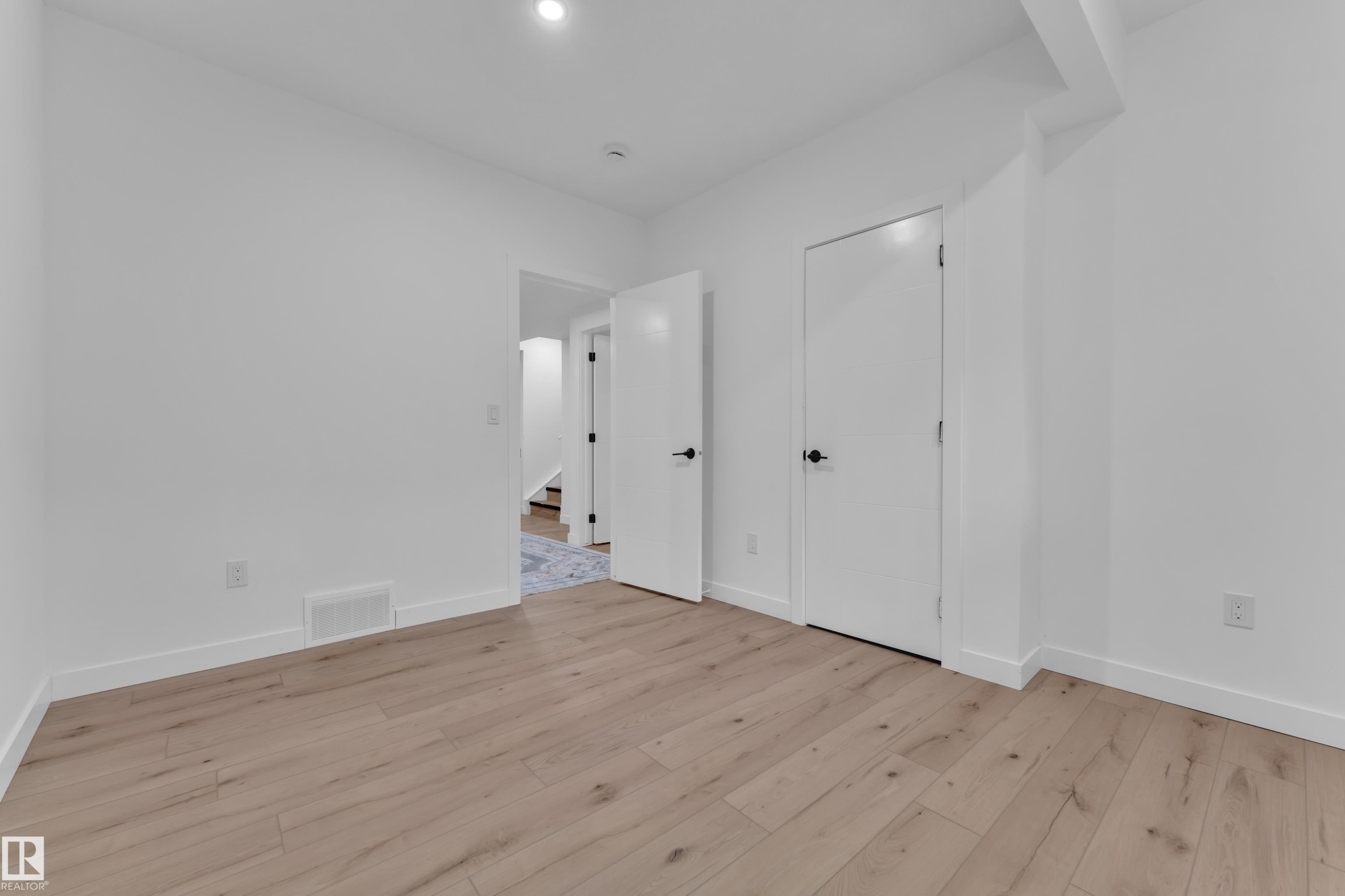 Spacious room featuring light wood-finish flooring, white baseboards, and a recessed ceiling light - 16816 49 Street, Edmonton, AB