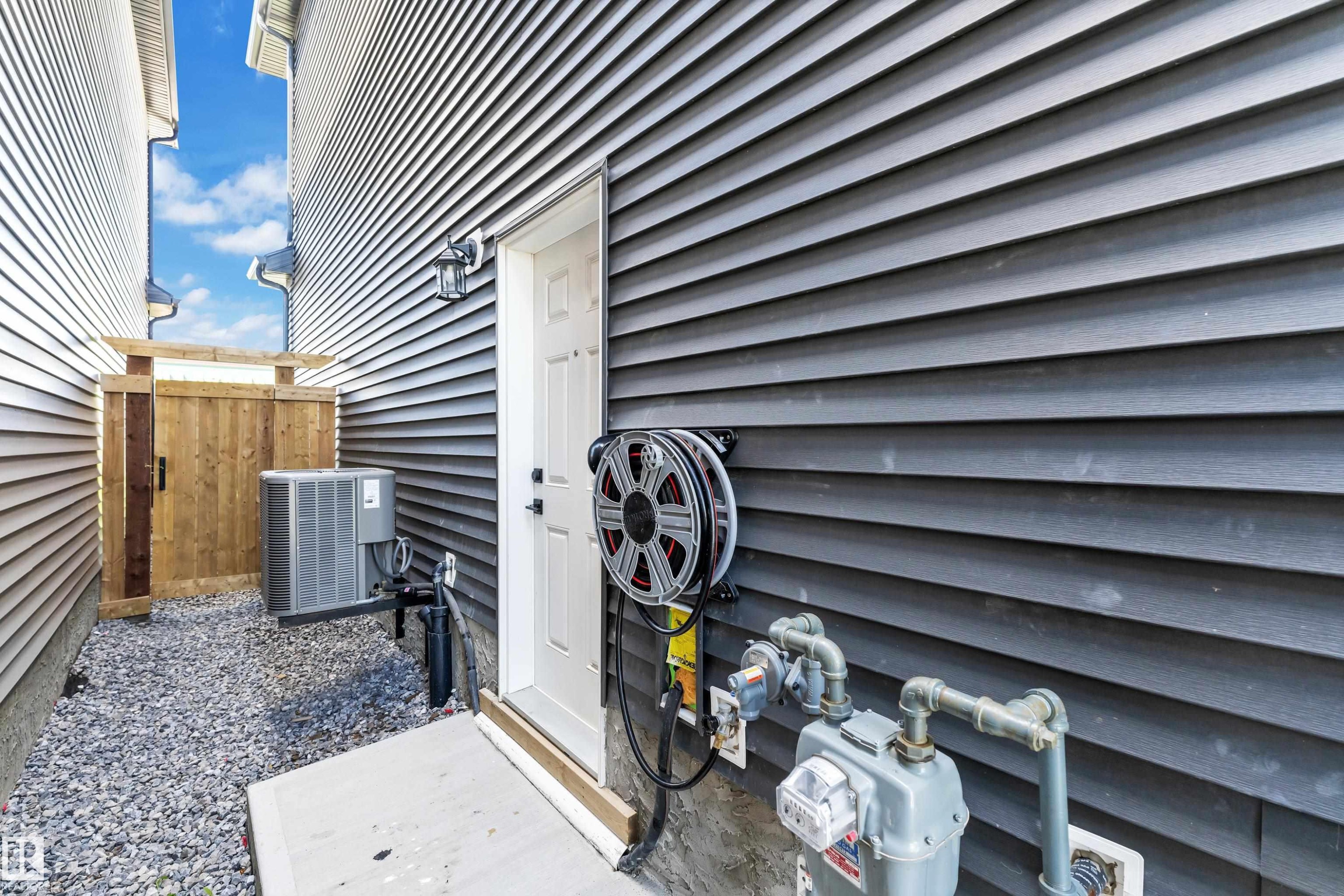Dark gray horizontal siding with a white utility door and exterior lighting fixture - 16816 49 Street, Edmonton, AB