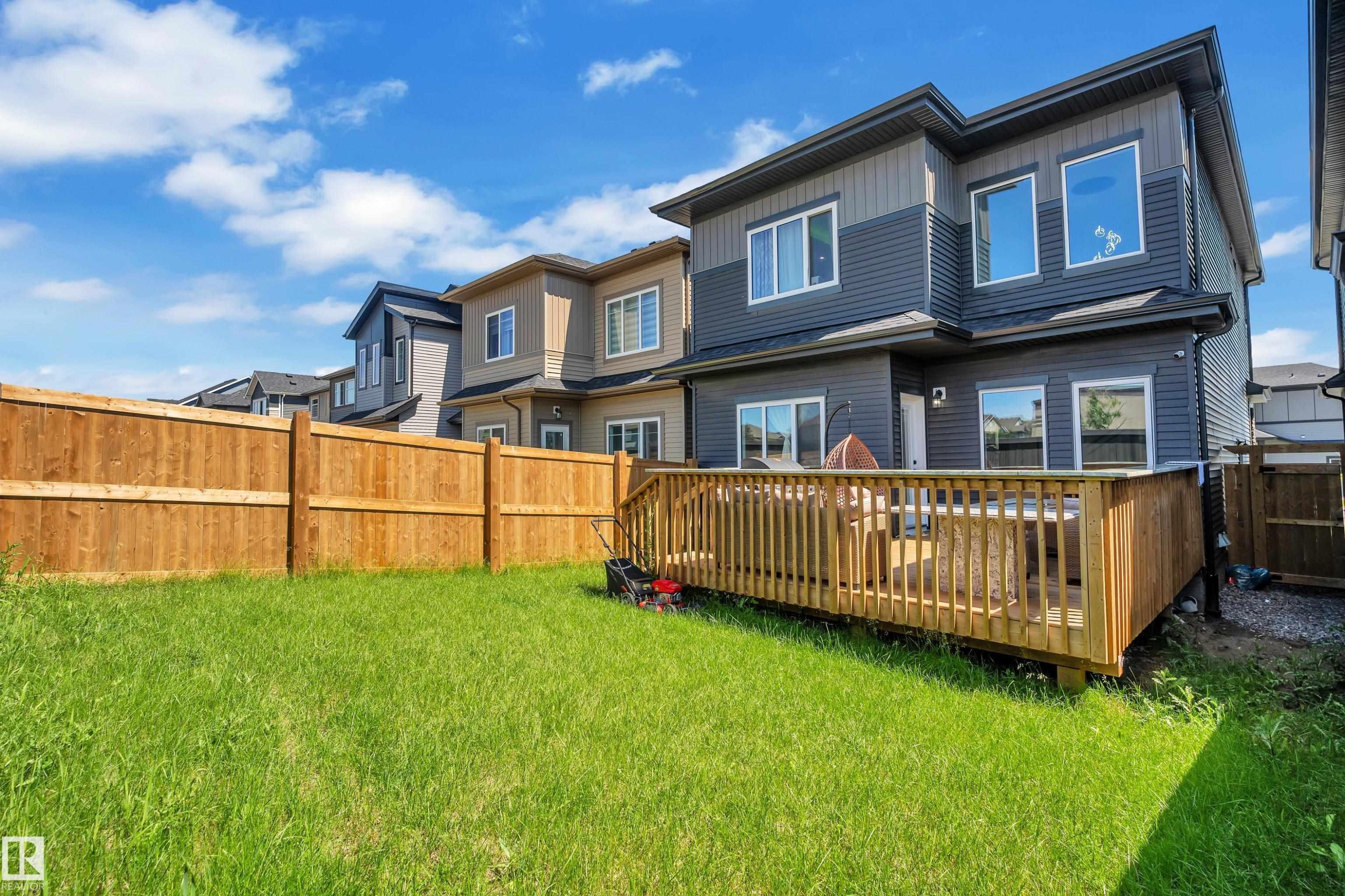 Rear exterior featuring a spacious wooden deck with railings, a grassy yard, and a full privacy fence - 16816 49 Street, Edmonton, AB