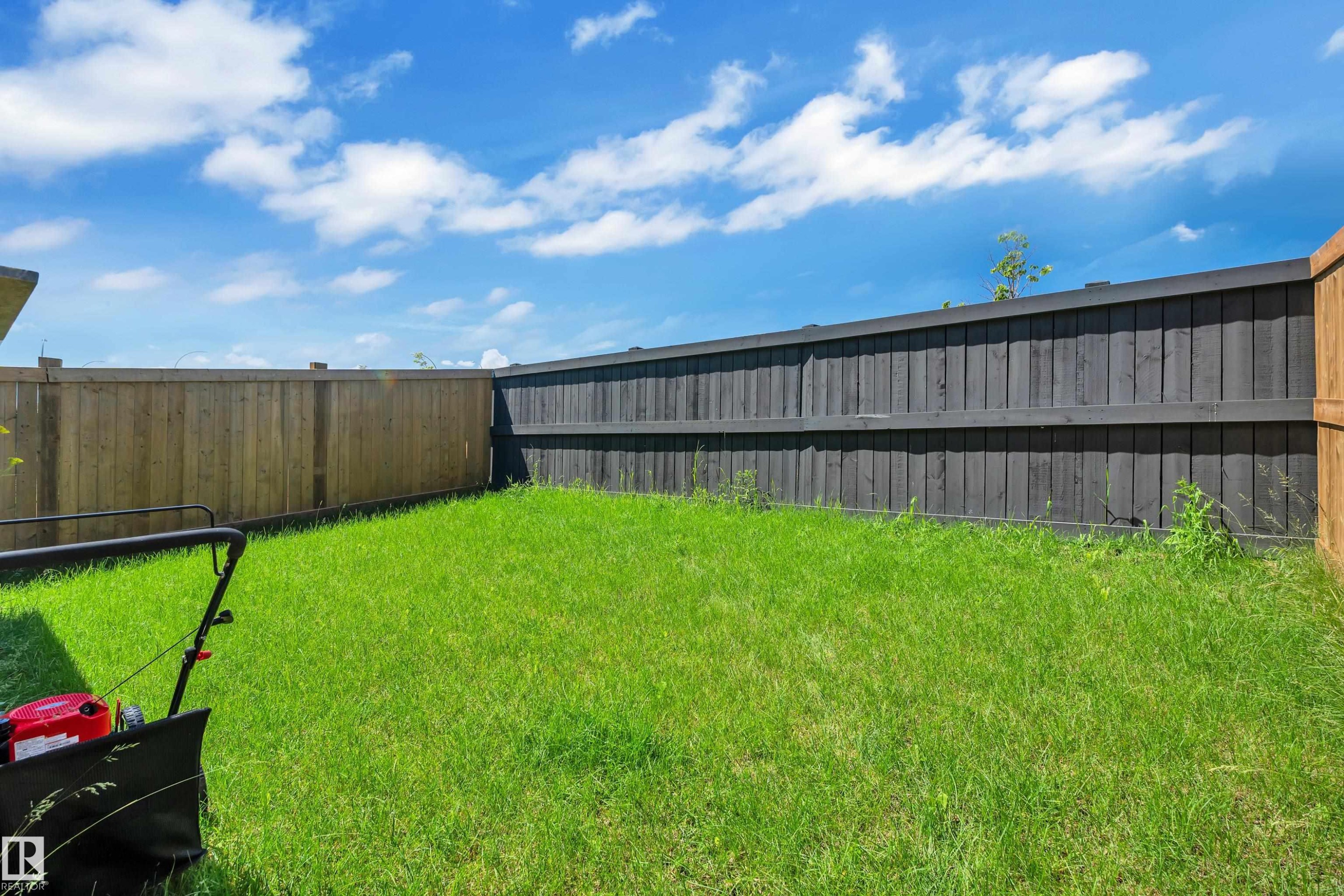 Fenced backyard featuring natural wood and dark-stained fencing, and a grassy lawn - 16816 49 Street, Edmonton, AB