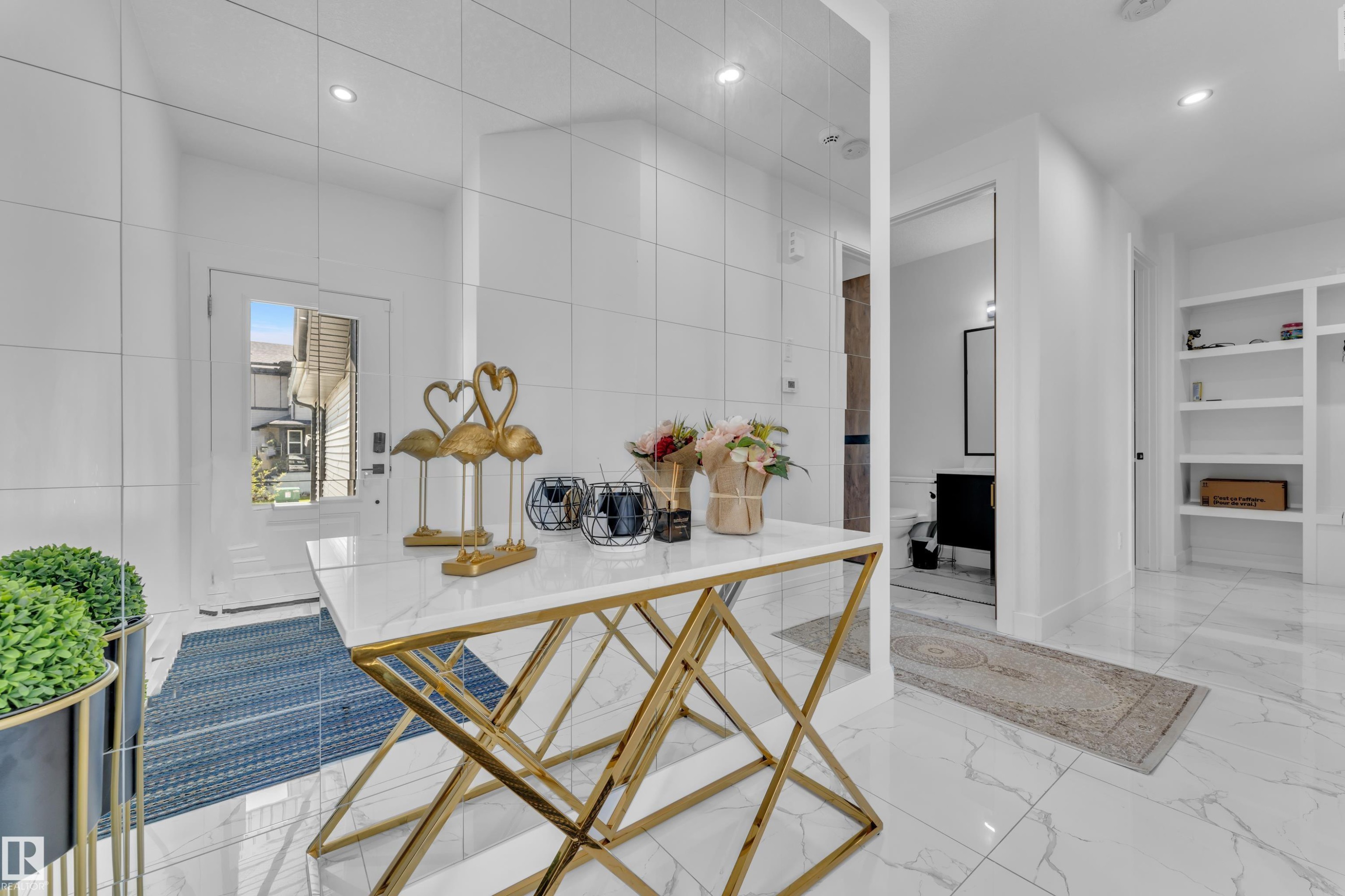 Bright entry foyer featuring large format white tile flooring, recessed lighting, a white paneled entry door with frosted glass, and built-in shelving - 16816 49 Street, Edmonton, AB