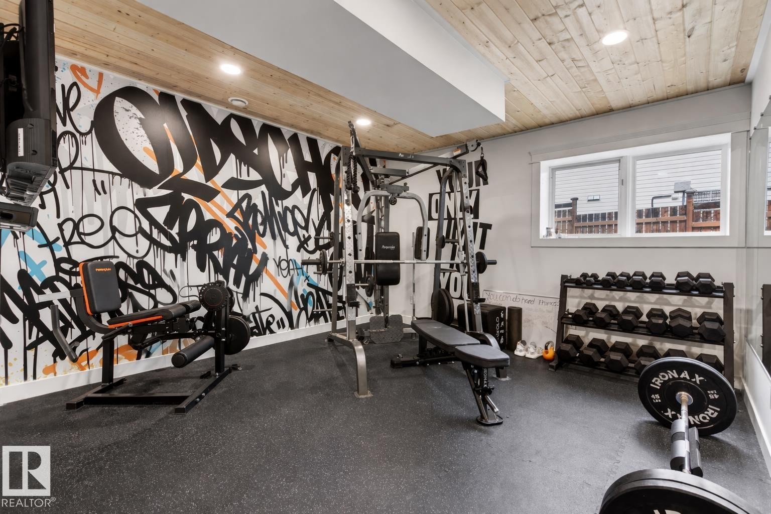 Dedicated fitness space featuring a graffiti-style accent wall, wood-finish ceiling, recessed lighting, and resilient rubber flooring - 711 Beach Avenue, Cold Lake, AB - Indoor Photo Showing Gym Room