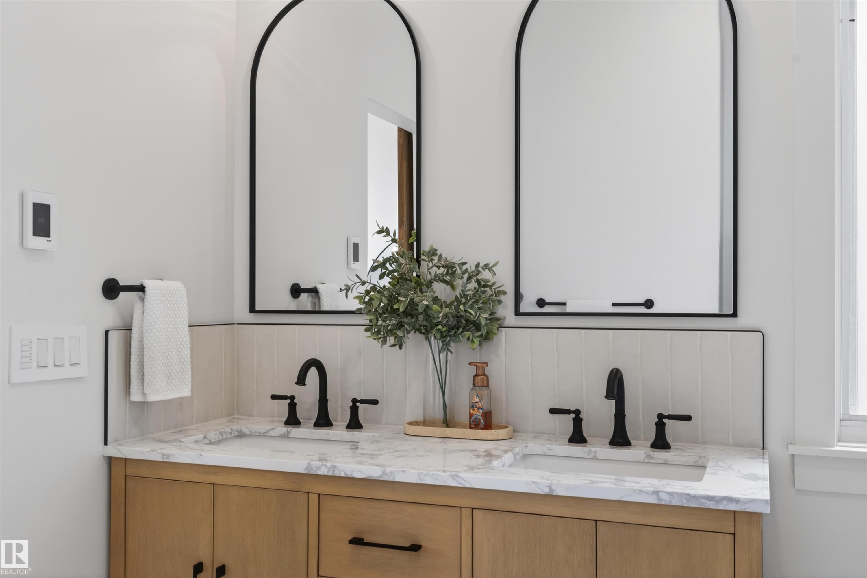 Dual arched mirrors with black frames complement the light wood-finish vanity featuring a stone countertop and integrated sinks - 711 Beach Avenue, Cold Lake, AB - Indoor Photo Showing Bathroom