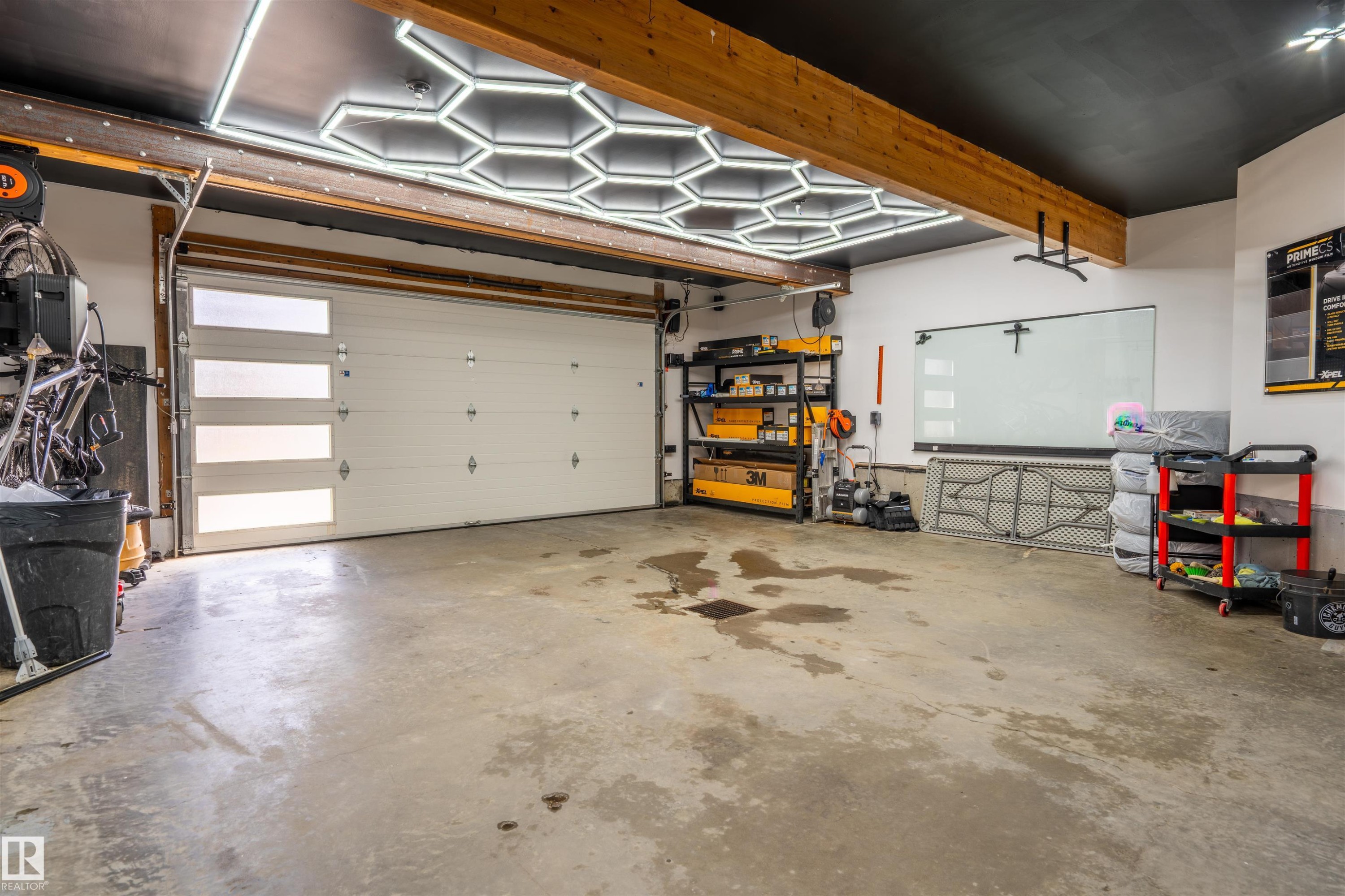 Garage featuring a modern white overhead door with horizontal frosted glass inserts, exposed wood ceiling beams, and contemporary hexagonal ceiling lighting - 711 Beach Avenue, Cold Lake, AB - Indoor Photo Showing Garage