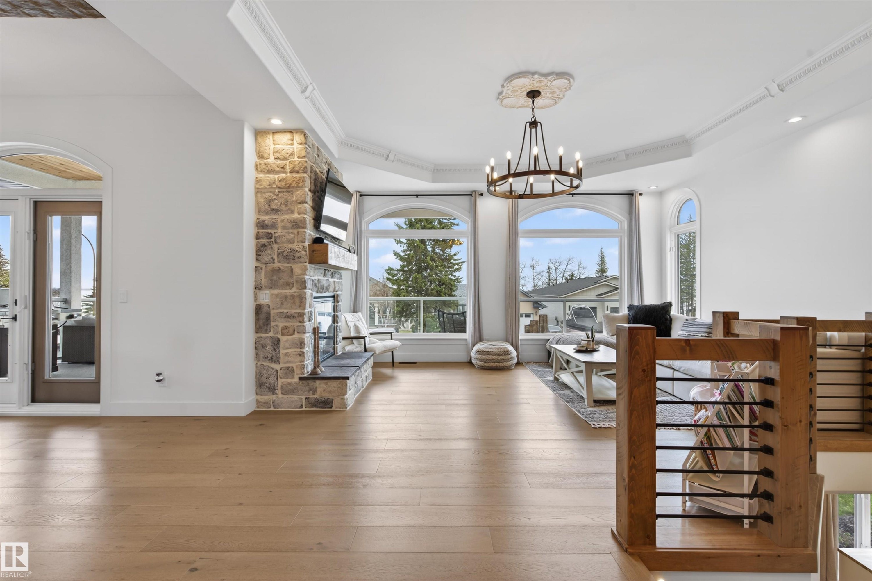Spacious room featuring light wood-finish flooring, a stone-clad fireplace with a hearth and wood mantel, and multiple arched windows - 711 Beach Avenue, Cold Lake, AB - Indoor