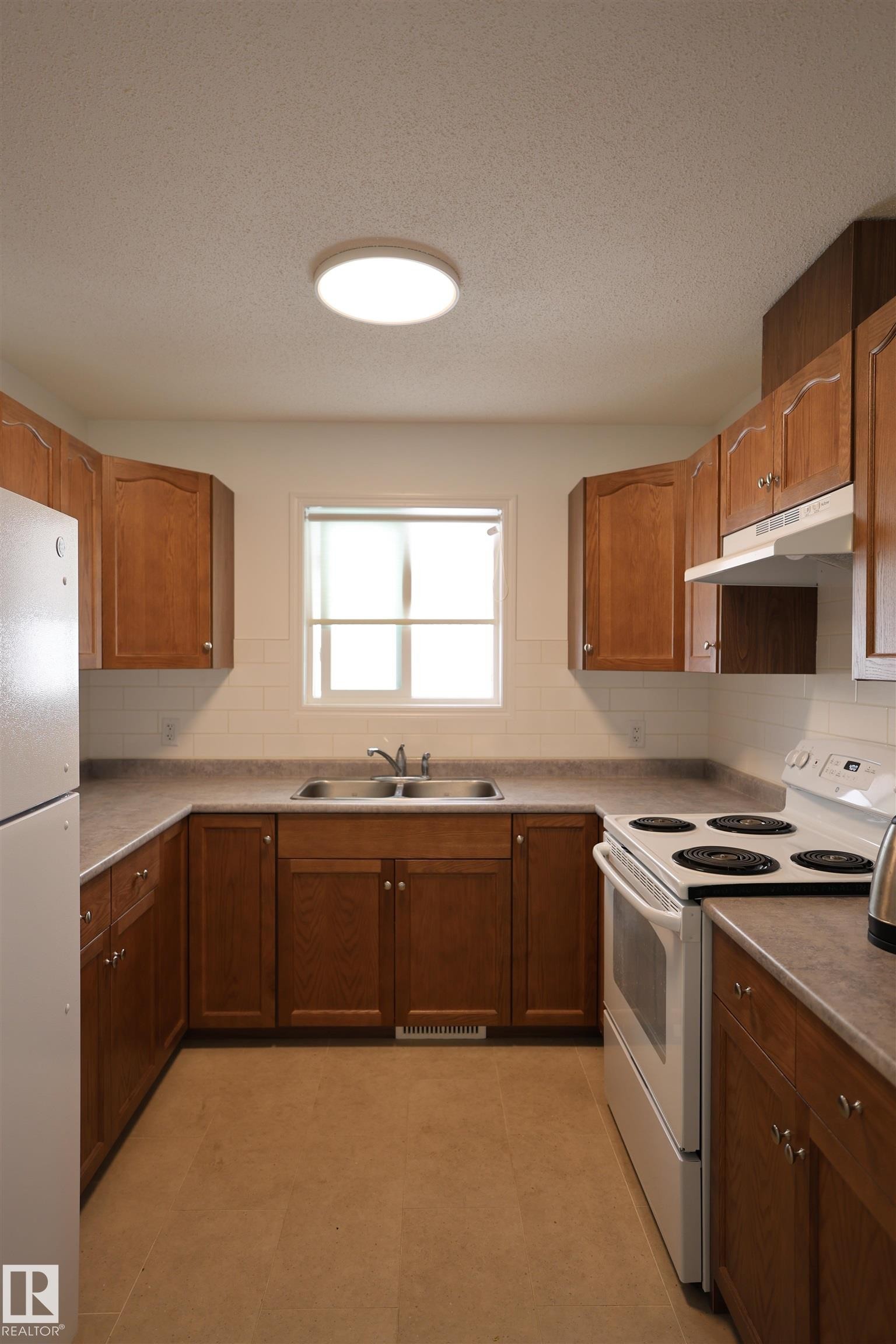 U-shaped kitchen featuring wood cabinetry, a double basin stainless steel sink, and light-toned countertops - 11120 132 Street, Edmonton, AB