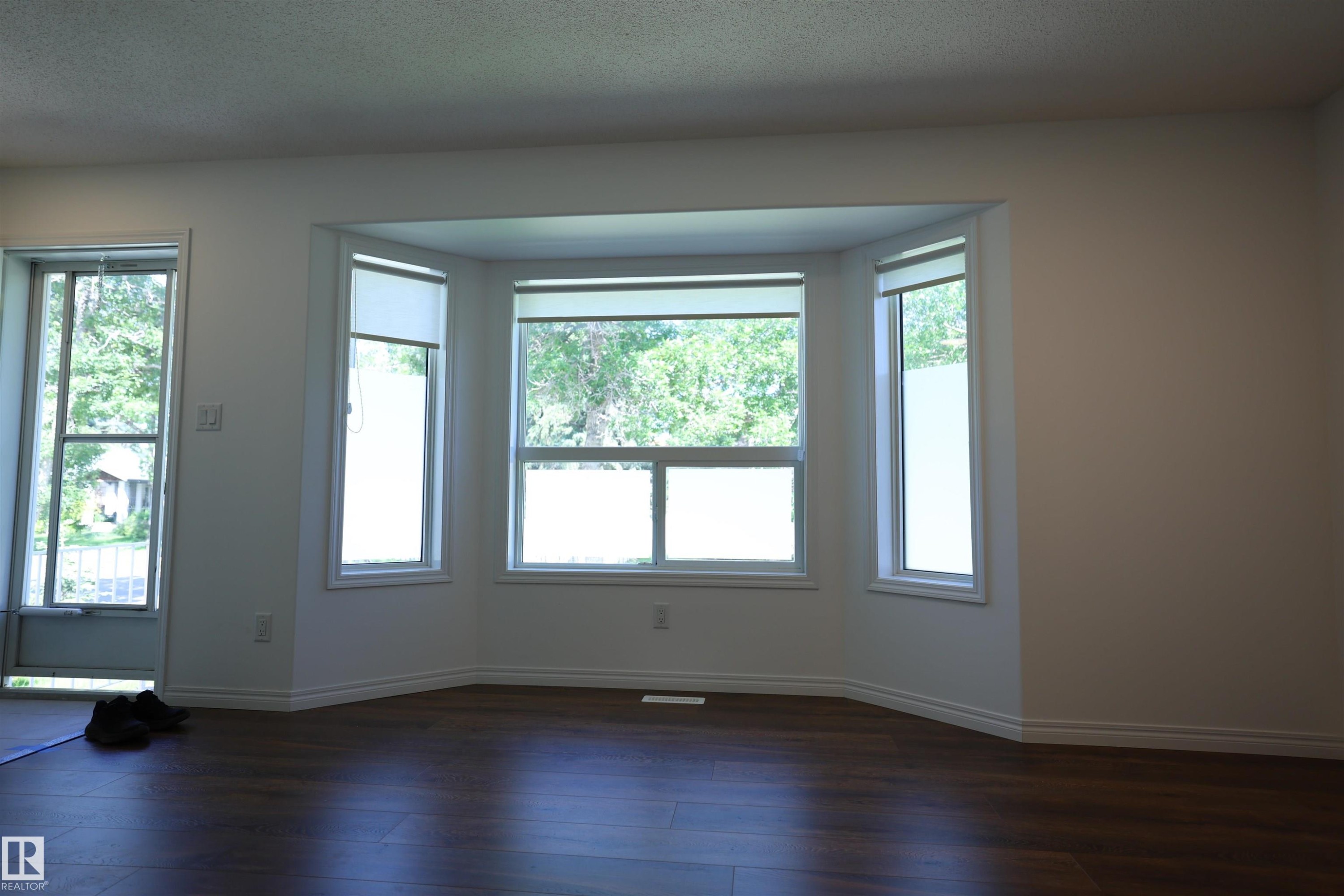 Spacious room featuring a bay window, wood-finish flooring, white walls, and white trim - 11120 132 Street, Edmonton, AB