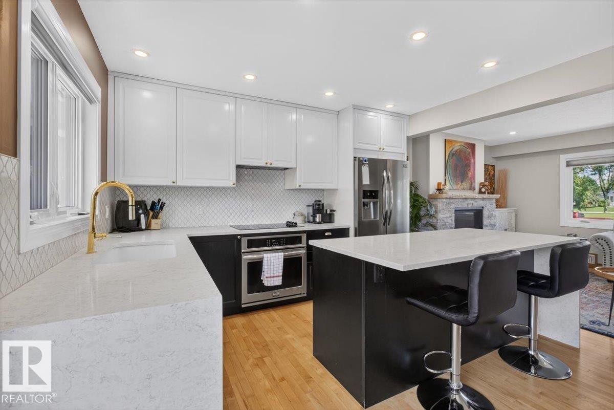 Modern kitchen featuring white upper cabinetry, black base cabinetry, a central island with countertop seating, stainless steel appliances, and a white diamond-patterned backsplash - 10736 48 Street Nw, Edmonton, AB - Indoor Photo Showing Kitchen With Upgraded Kitchen