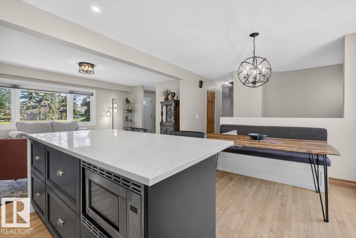 Kitchen island with a light-toned countertop and built-in microwave, dark cabinetry with decorative hardware, and light wood-finish flooring - 10736 48 Street Nw, Edmonton, AB - Indoor Photo Showing Other Room
