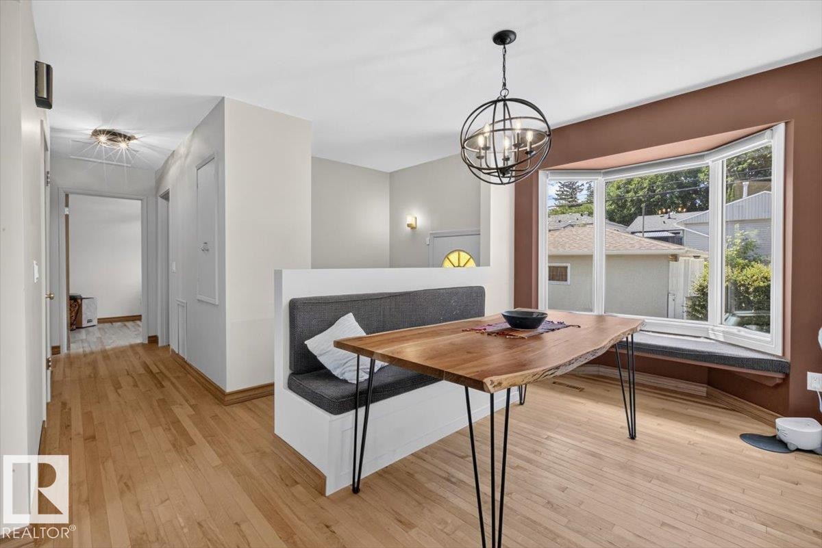 Hardwood flooring extends throughout this interior space featuring a built-in banquette, a bay window with integrated seating, and a modern spherical chandelier - 10736 48 Street Nw, Edmonton, AB - Indoor