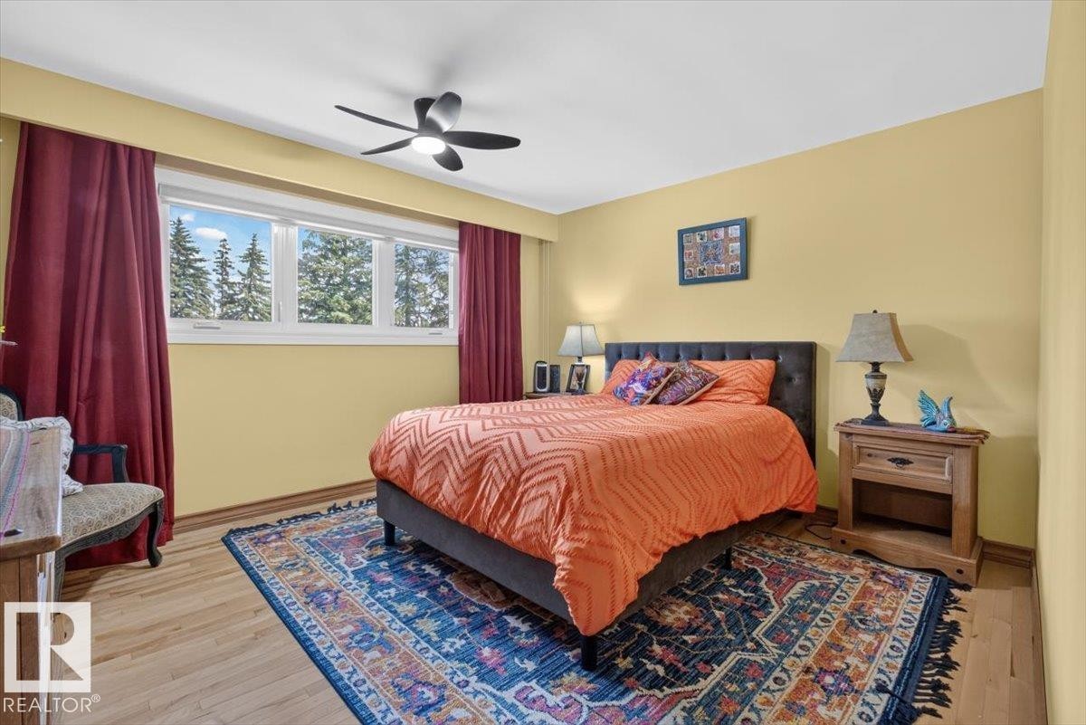 Spacious bedroom featuring wood-finish flooring, a contemporary ceiling fan with integrated lighting, and multiple windows providing natural light - 10736 48 Street Nw, Edmonton, AB - Indoor Photo Showing Bedroom