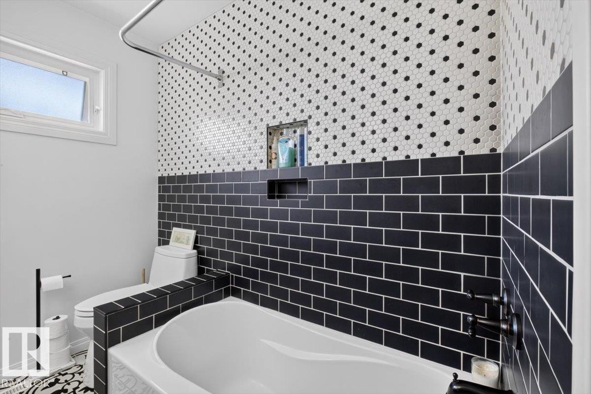 Bathroom featuring a white soaking tub with matte black fixtures, black subway tile, and white hexagonal tile with black accents - 10736 48 Street Nw, Edmonton, AB - Indoor Photo Showing Bathroom