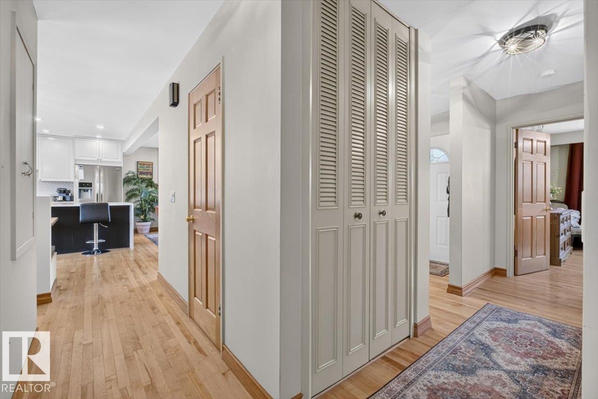 Hardwood flooring throughout the hallway, leading to a kitchen with white cabinetry and a black island with a breakfast bar - 10736 48 Street Nw, Edmonton, AB - Indoor Photo Showing Other Room
