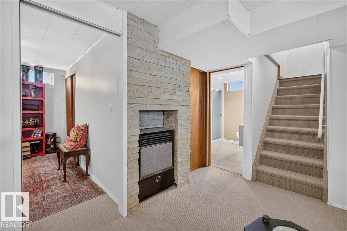 Carpeted flooring throughout a finished lower level featuring a brick-style facade surrounding a built-in furnace unit - 10736 48 Street Nw, Edmonton, AB - Indoor With Fireplace