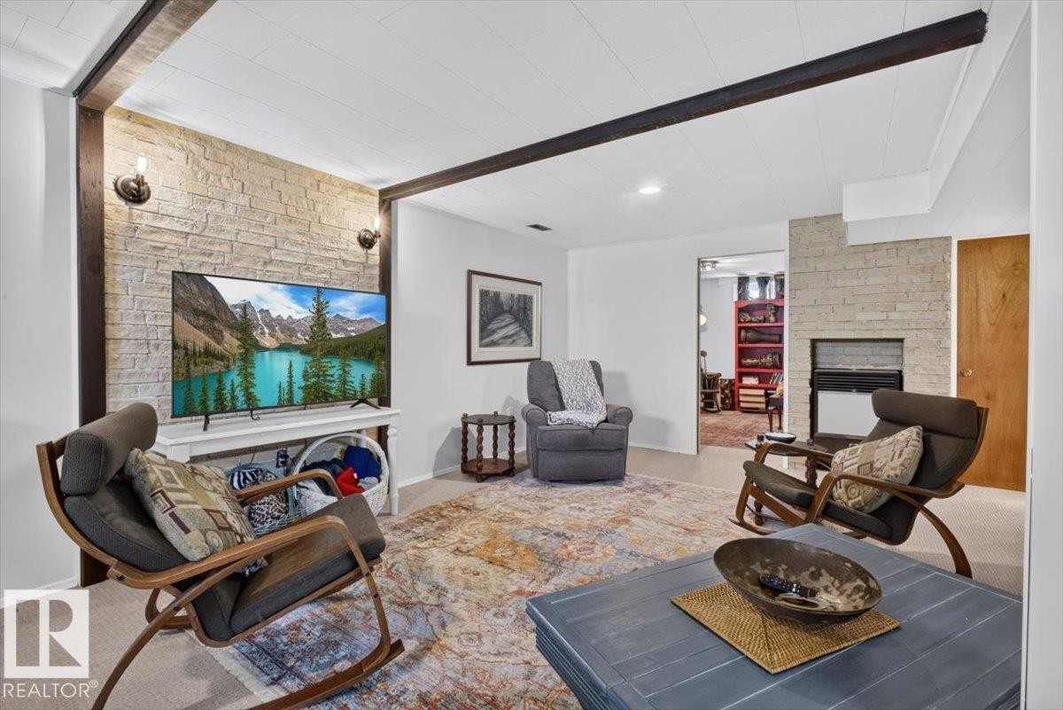 Recreational space featuring a stone accent wall, exposed ceiling beams, and a fireplace with a black insert - 10736 48 Street Nw, Edmonton, AB - Indoor Photo Showing Living Room With Fireplace
