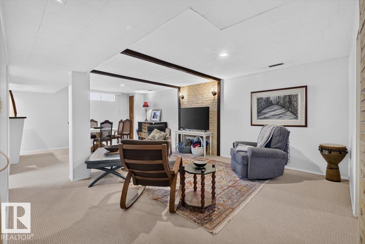 Carpeted lower-level living area featuring exposed wood beams, recessed lighting, and a partial brick accent wall - 10736 48 Street Nw, Edmonton, AB - Indoor