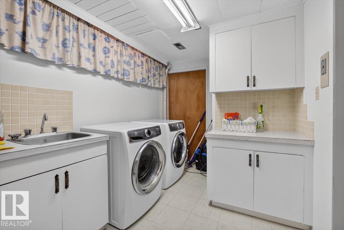 Dedicated laundry area featuring a utility sink, white cabinetry with storage, and a tiled backsplash - 10736 48 Street Nw, Edmonton, AB - Indoor Photo Showing Laundry Room