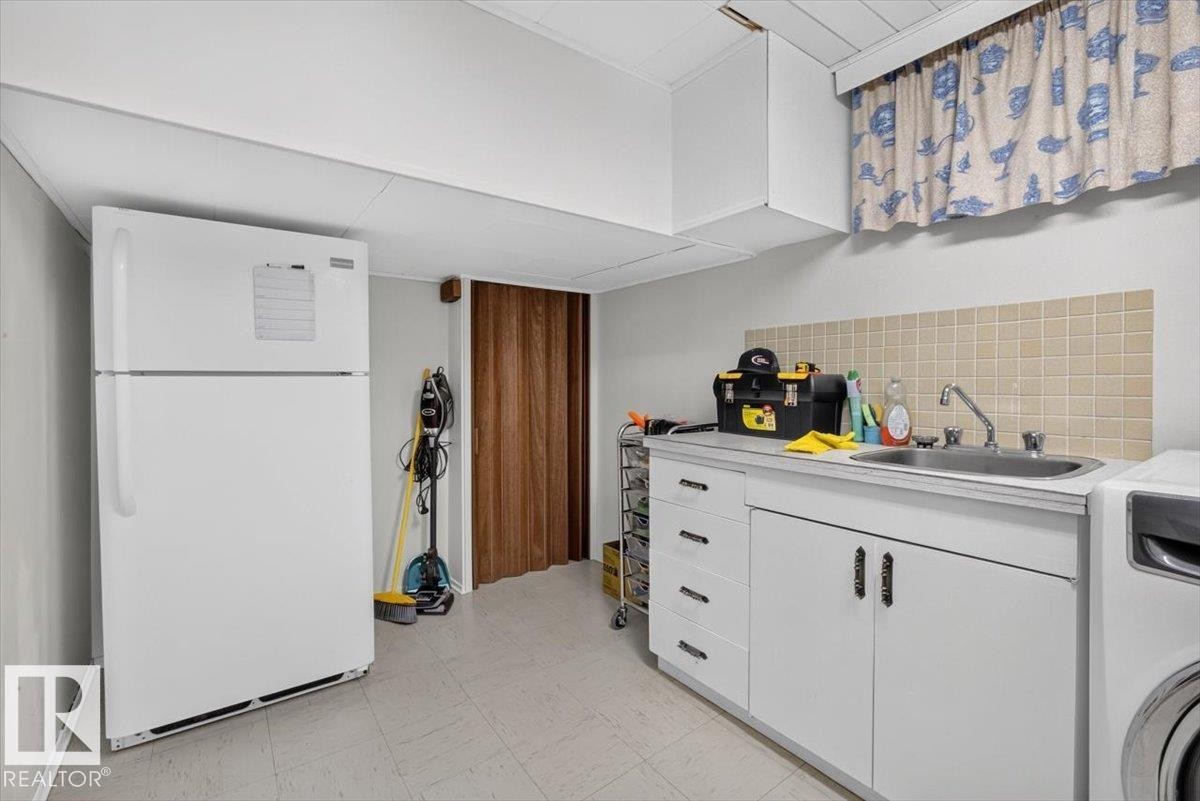 Utility area featuring a built-in sink with a tiled backsplash, white cabinetry with silver hardware, and durable flooring - 10736 48 Street Nw, Edmonton, AB - Indoor Photo Showing Laundry Room