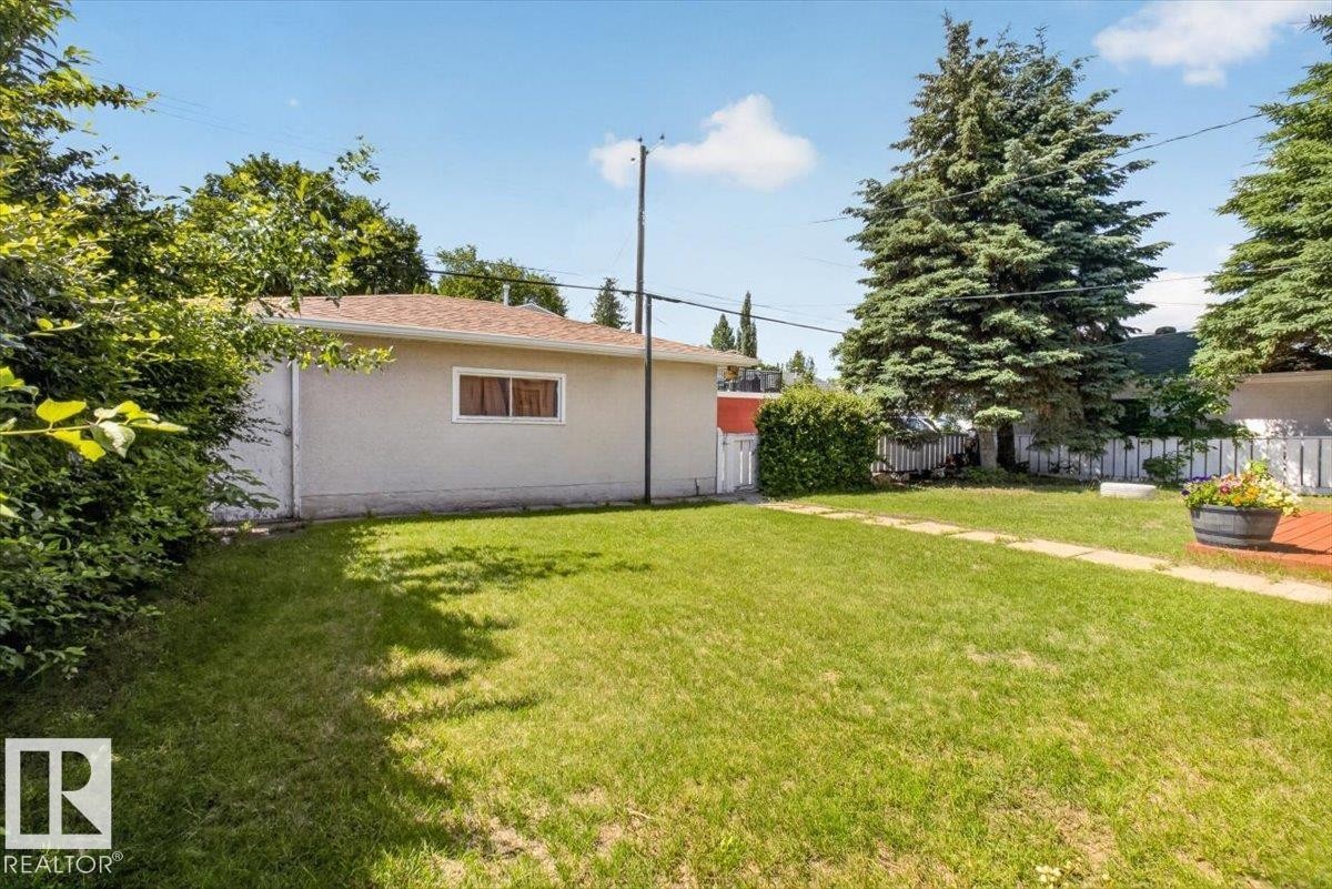 Expansive rear yard featuring a manicured lawn, established landscaping, and a stucco exterior structure with a brown shingle roof - 10736 48 Street Nw, Edmonton, AB - Outdoor