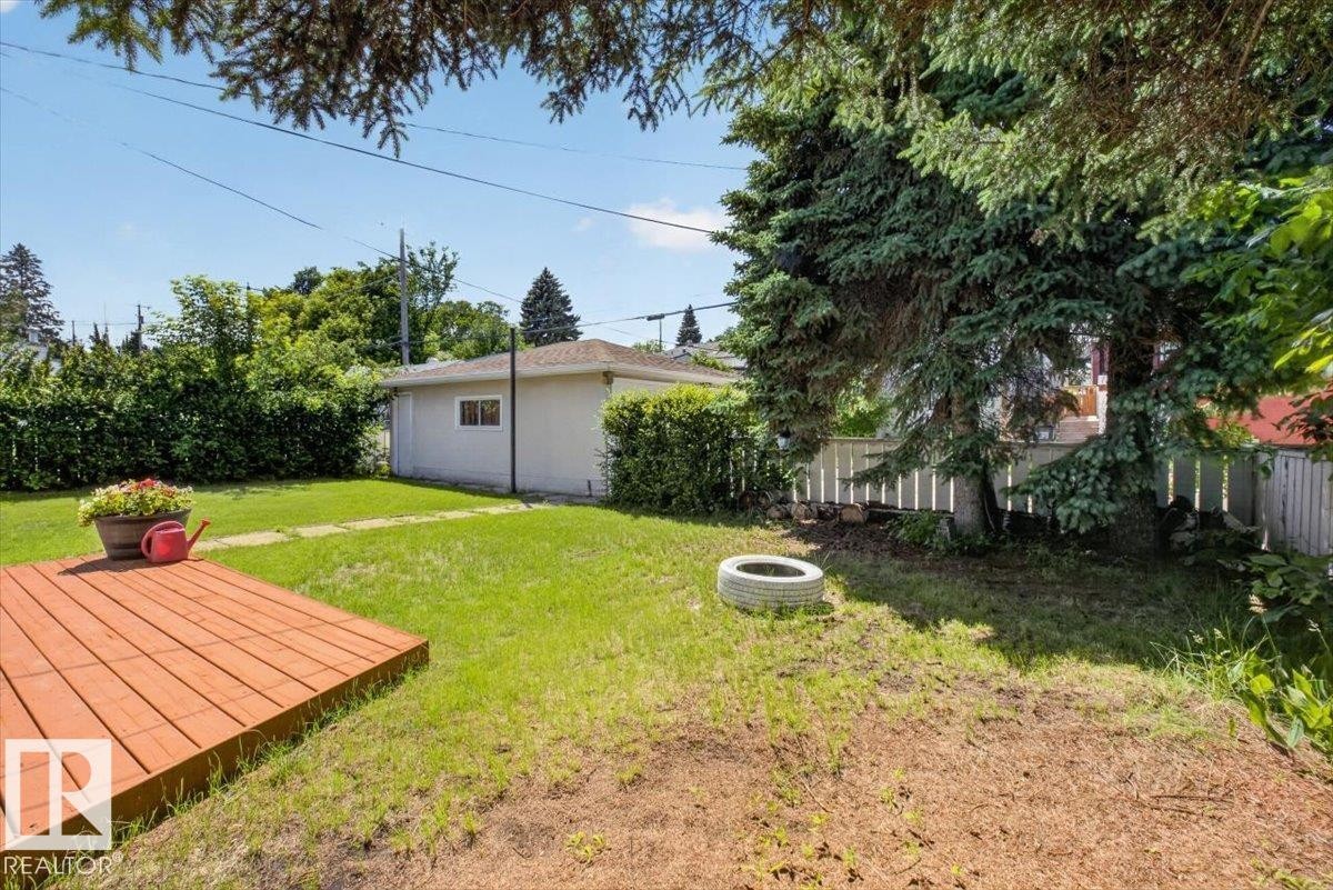 Expansive backyard featuring a wood deck, manicured lawn, and mature evergreen trees - 10736 48 Street Nw, Edmonton, AB - Outdoor