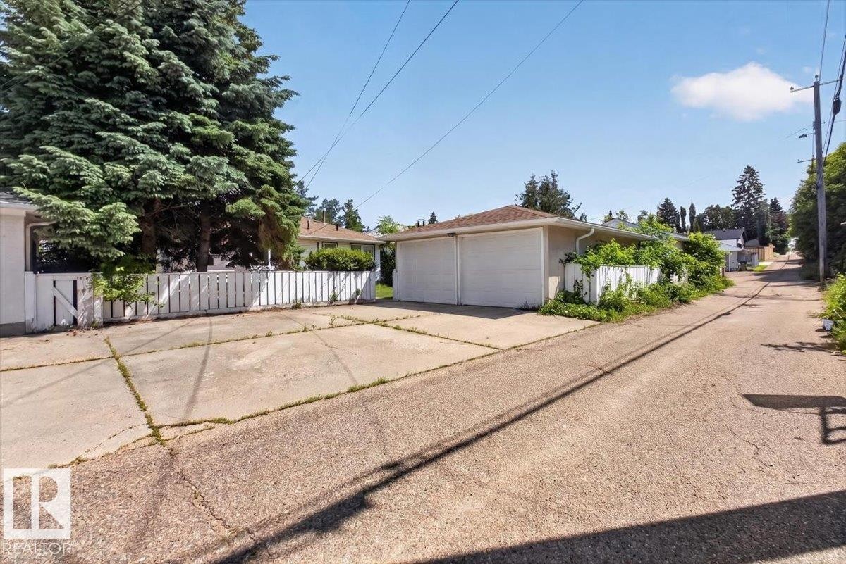 Exterior featuring a two-car garage with white doors, white picket fencing, and mature evergreen trees - 10736 48 Street Nw, Edmonton, AB - Outdoor