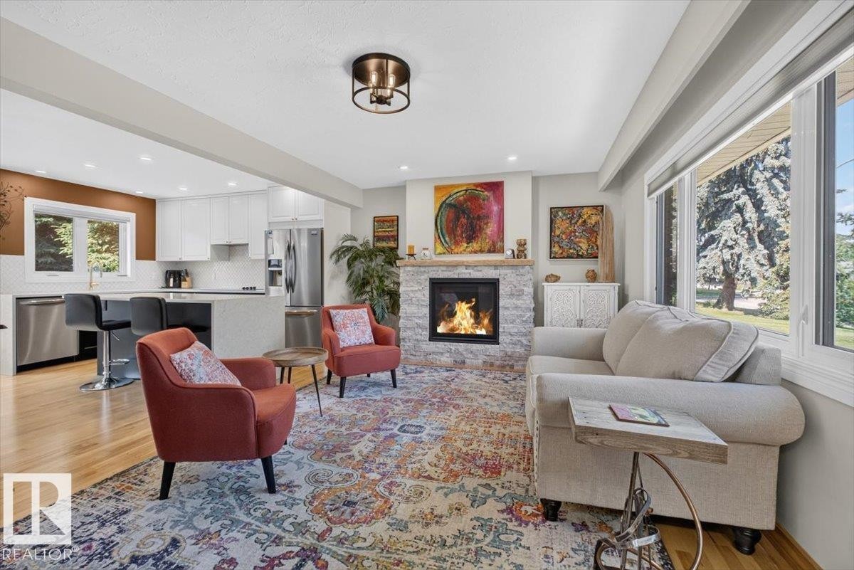 Open-concept living space featuring a stacked stone fireplace, wood-finish flooring, large windows, and recessed lighting - 10736 48 Street Nw, Edmonton, AB - Indoor Photo Showing Living Room With Fireplace