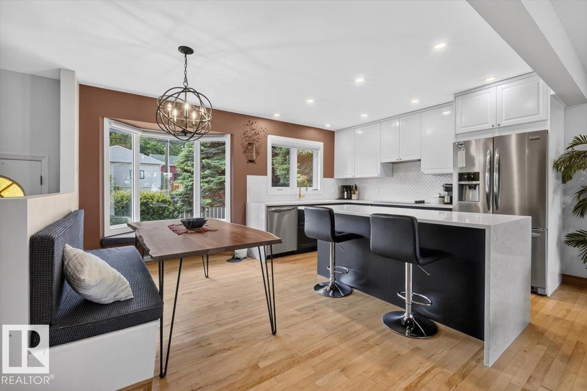 Kitchen featuring light wood-finish flooring, white upper cabinetry, and dark lower cabinetry with a waterfall-edge countertop island - 10736 48 Street Nw, Edmonton, AB - Indoor Photo Showing Kitchen With Upgraded Kitchen