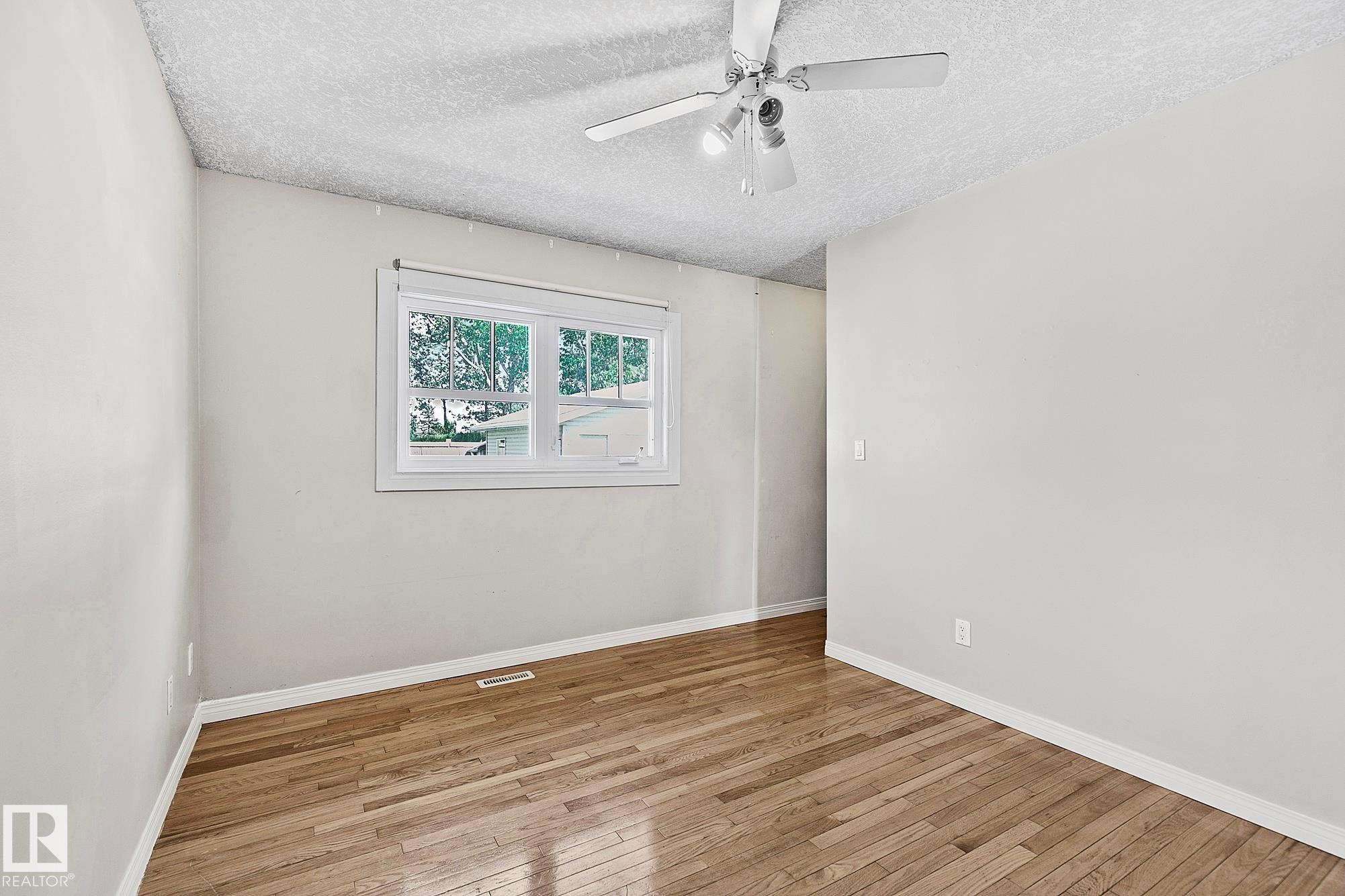 Room featuring wood-finish flooring, a window with exterior views, light-toned wall paint, and a ceiling fan with integrated lighting - 17059 98 Street, Edmonton, AB - Indoor Photo Showing Other Room