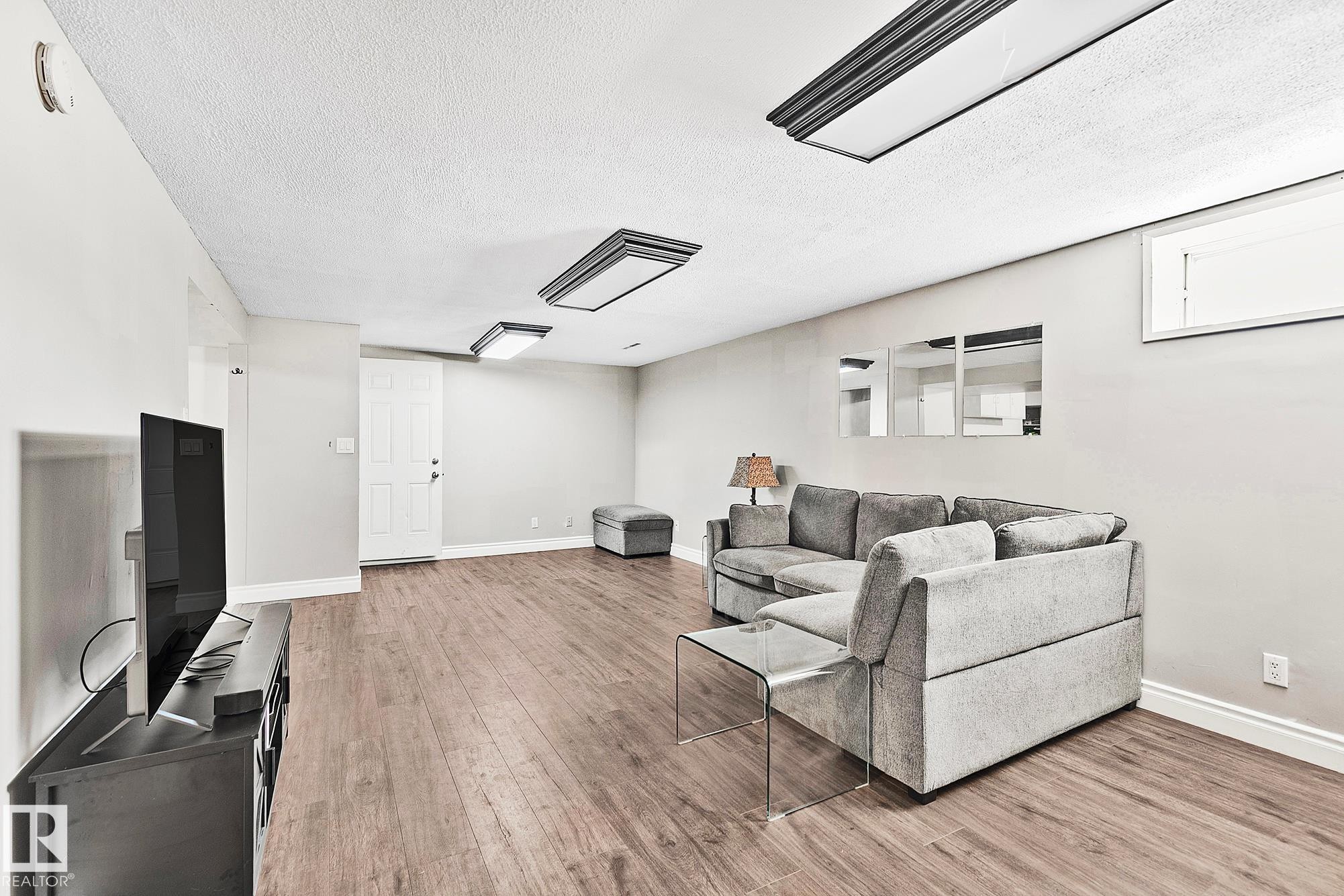 Spacious room featuring wood-finish flooring, light gray walls, and recessed ceiling lighting - 17059 98 Street, Edmonton, AB - Indoor